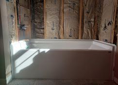 White bathtub installed in a bathroom under construction, surrounded by insulation and wooden framing.