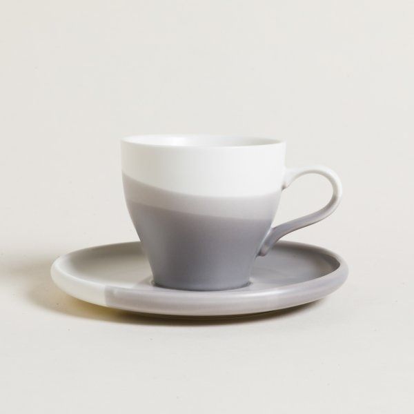 Una taza de café gris y blanca sobre un platillo.
