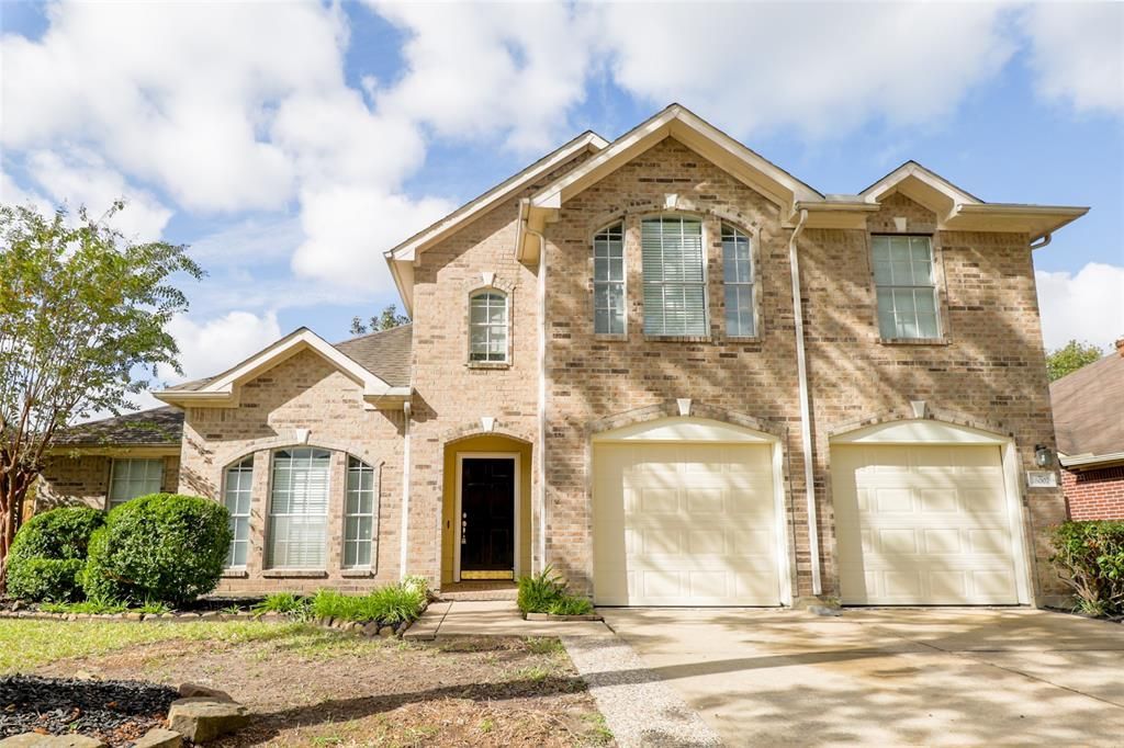 Two-story brick house with a two-car garage under a cloudy sky.