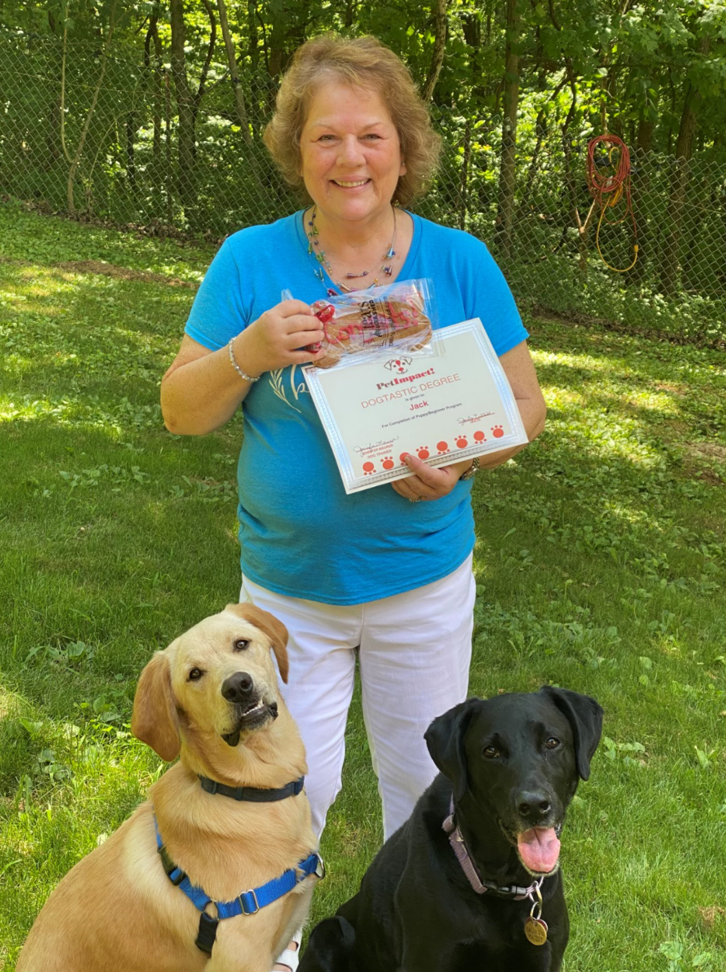 Woman holding a box of treats with two dogs sitting in front of her outside.