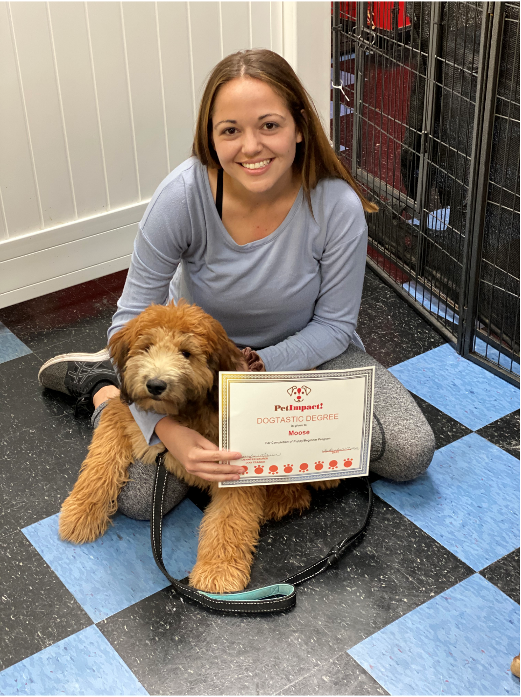 Woman and Goldendoodle dog holding a certificate, sitting on a blue and black checkered floor.