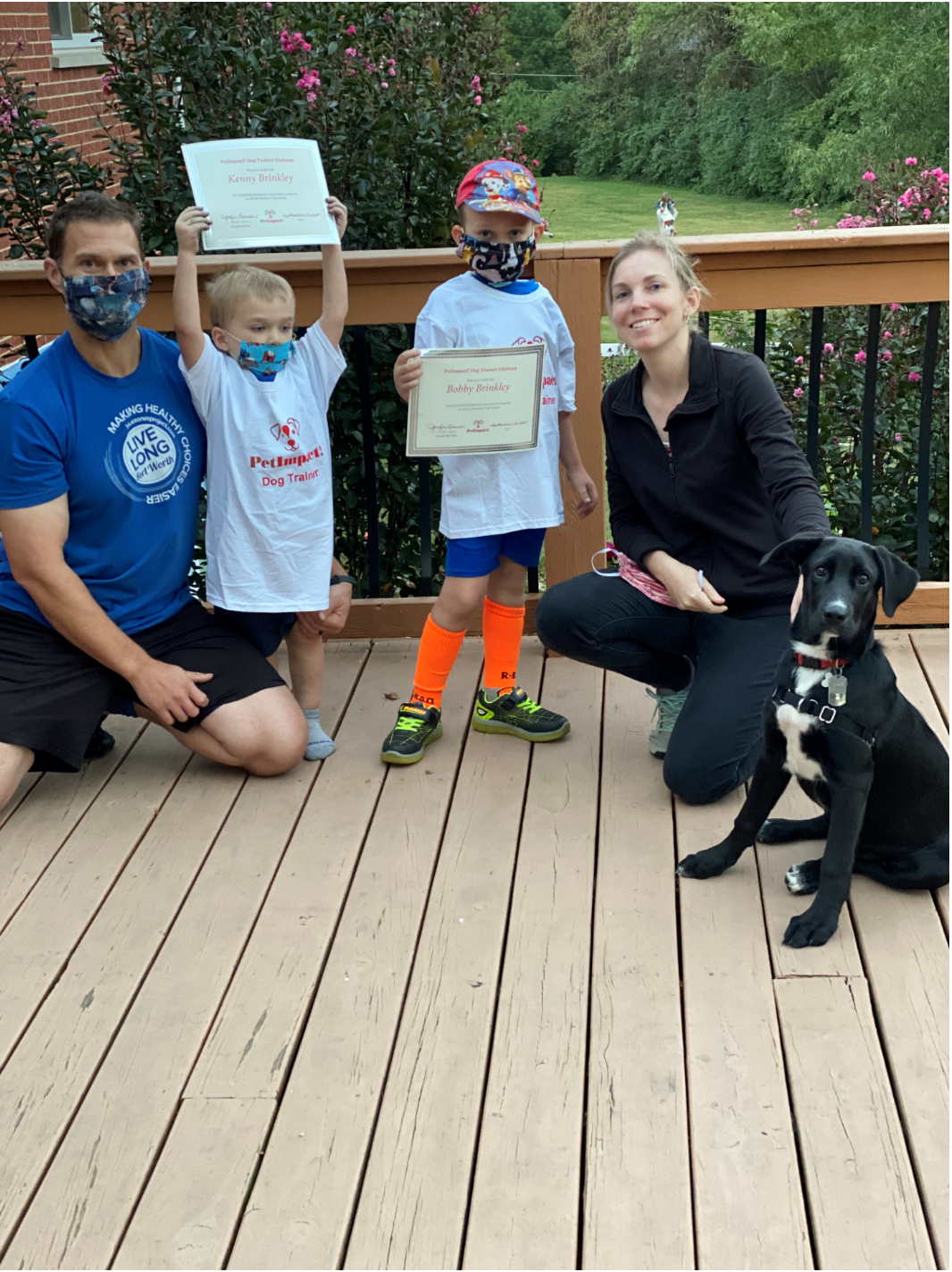 Family on deck with children holding certificates; dog sits beside woman.