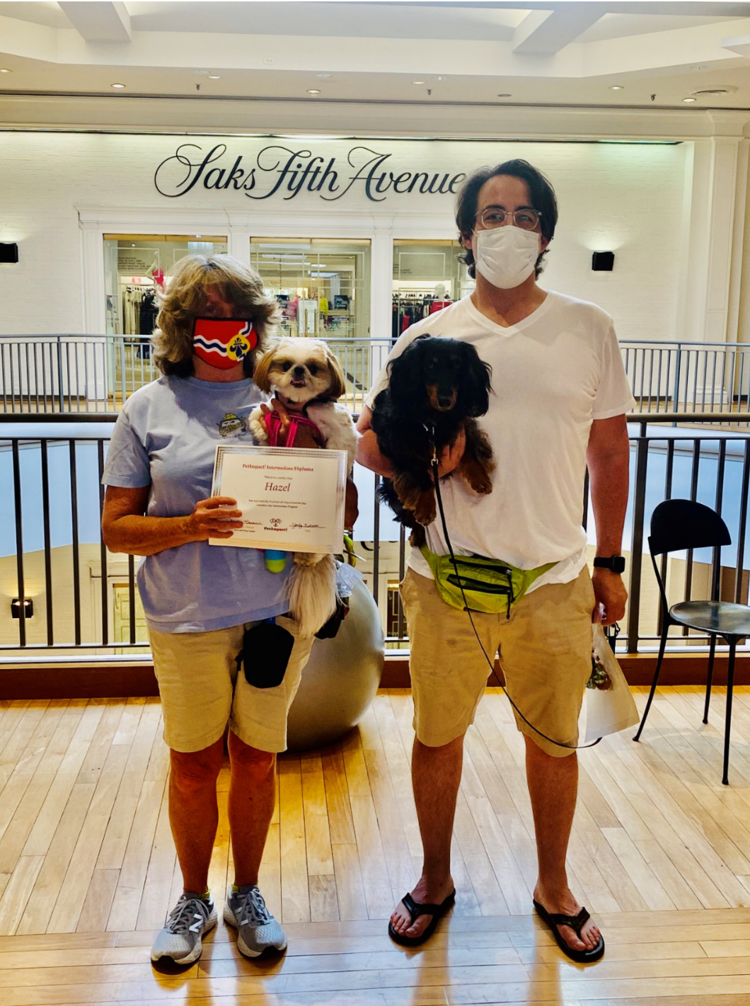 Two people with dogs in front of Saks Fifth Avenue store. Woman holds a dog and a certificate, the man holds another dog.