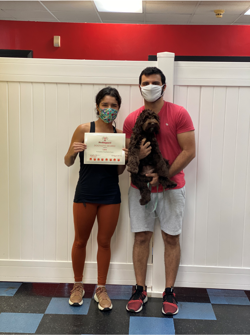 Woman and man with a dog and certificate in a room. All wearing masks.