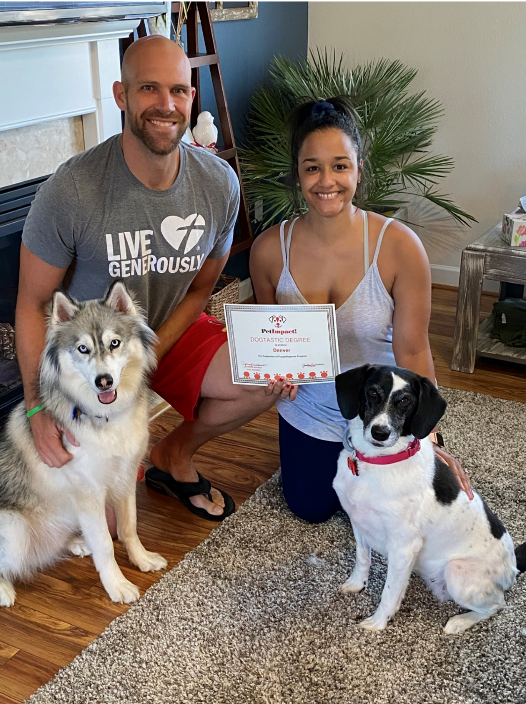 Man and woman kneeling with two dogs, holding a certificate.