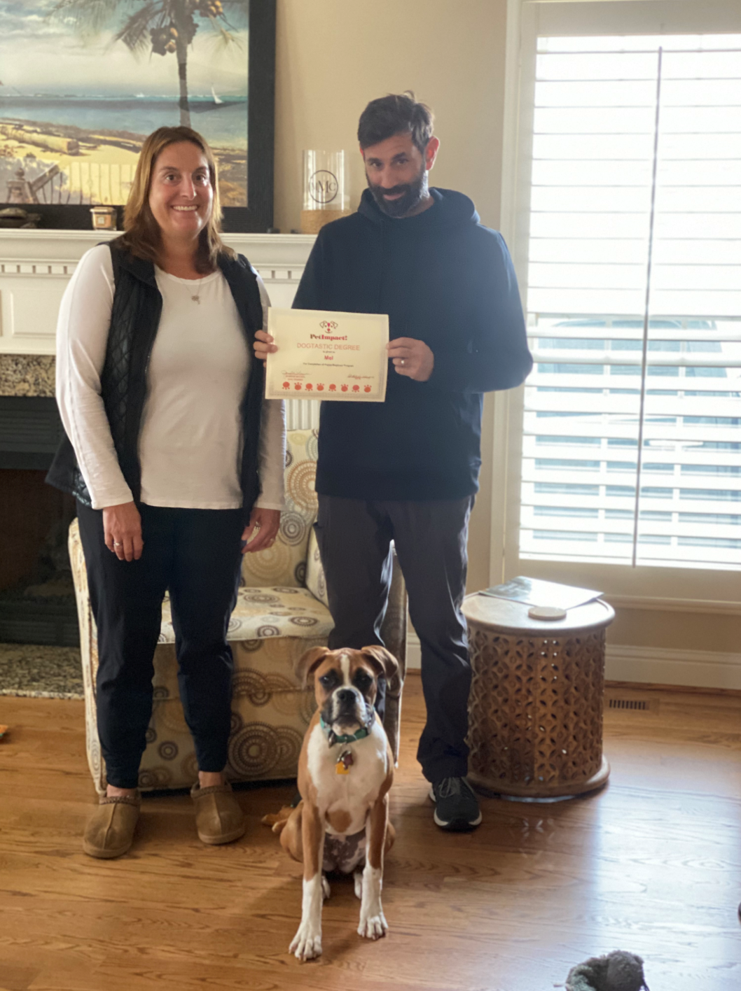 Woman and man holding certificate with a dog in front of them in a living room.