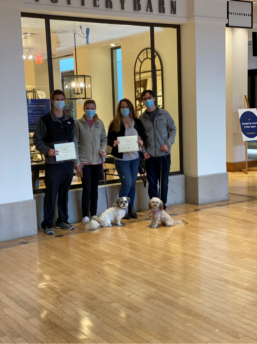 Four people with dogs in front of Pottery Barn, each holding a certificate.