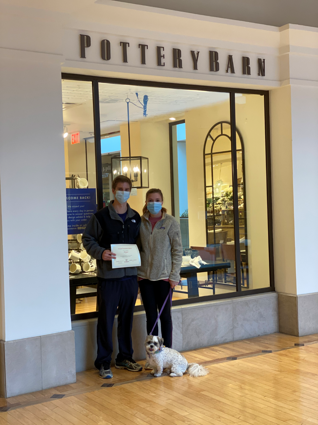 Two people with a dog pose in front of a Pottery Barn store. They hold a document.