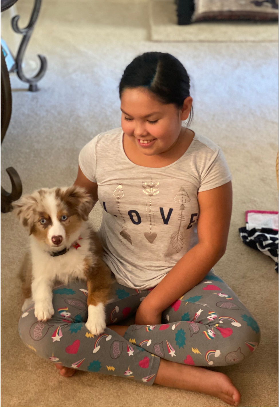 Girl sitting on floor with small, tri-color dog. Girl is smiling, wearing pajamas.