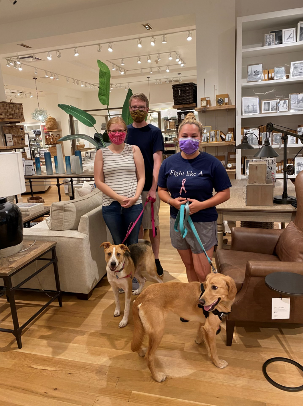 Three people with two dogs inside a home goods store; all wearing masks.