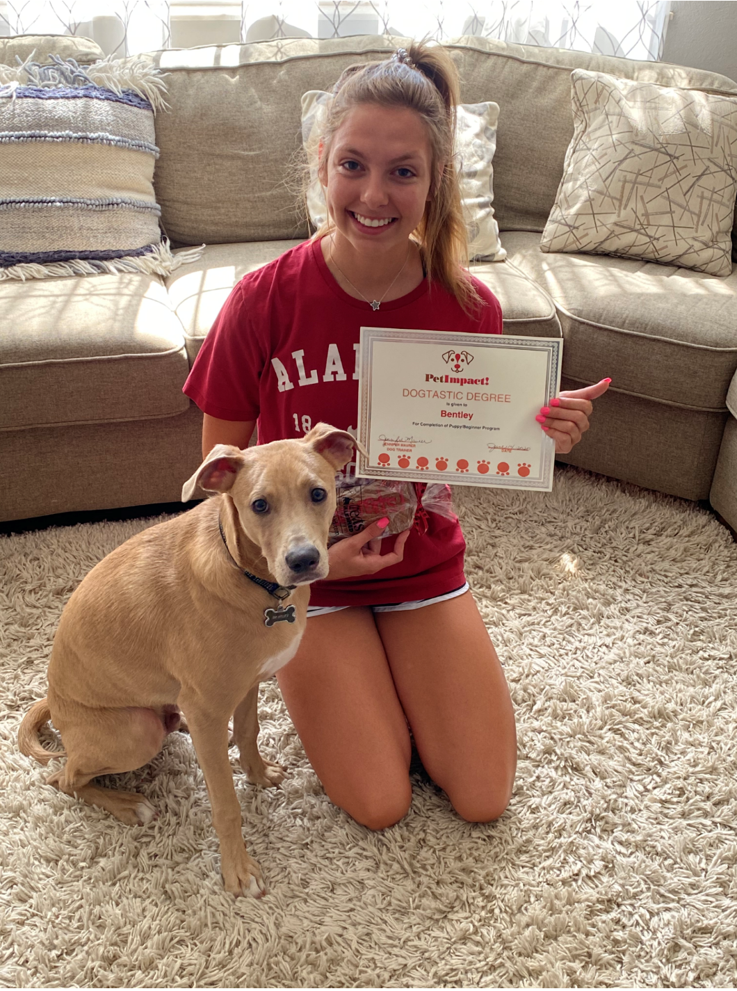 Woman and dog sitting on carpet, woman holding award.