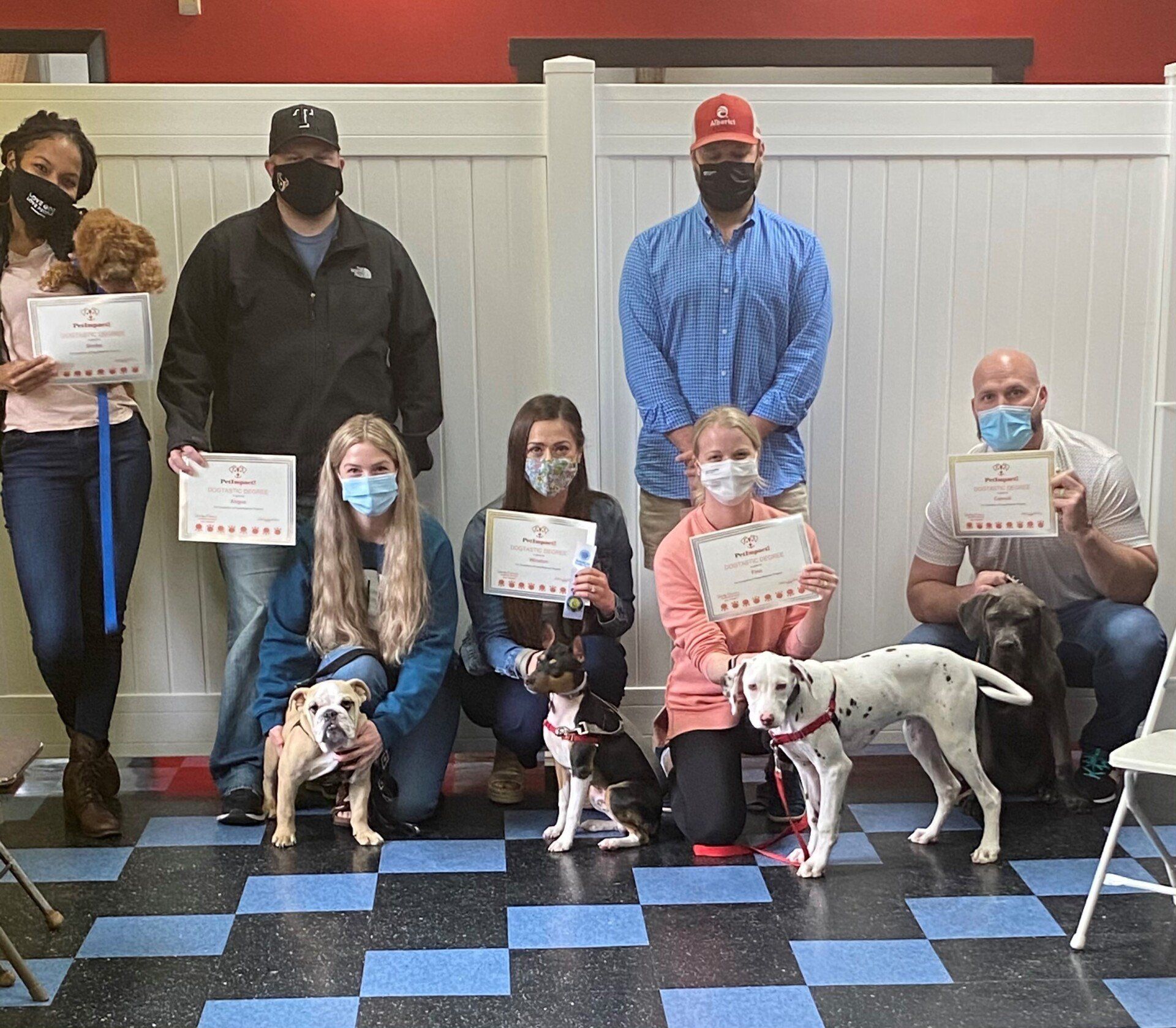 Group of people with dogs holding certificates in a training room.