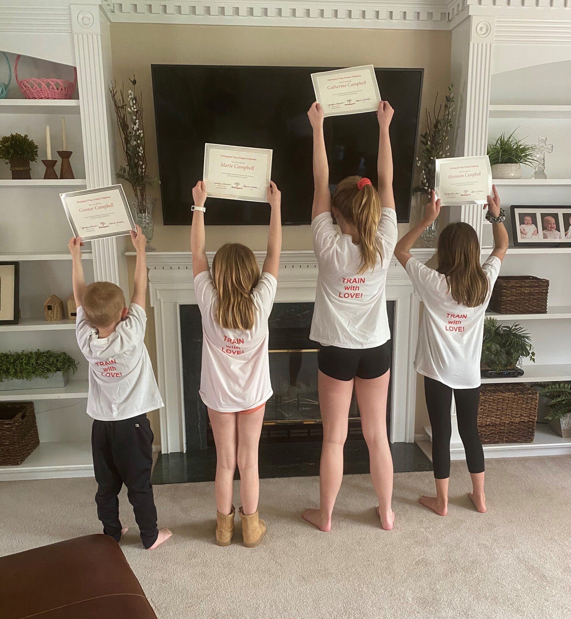 Four children holding papers up, standing in front of a fireplace in a living room.