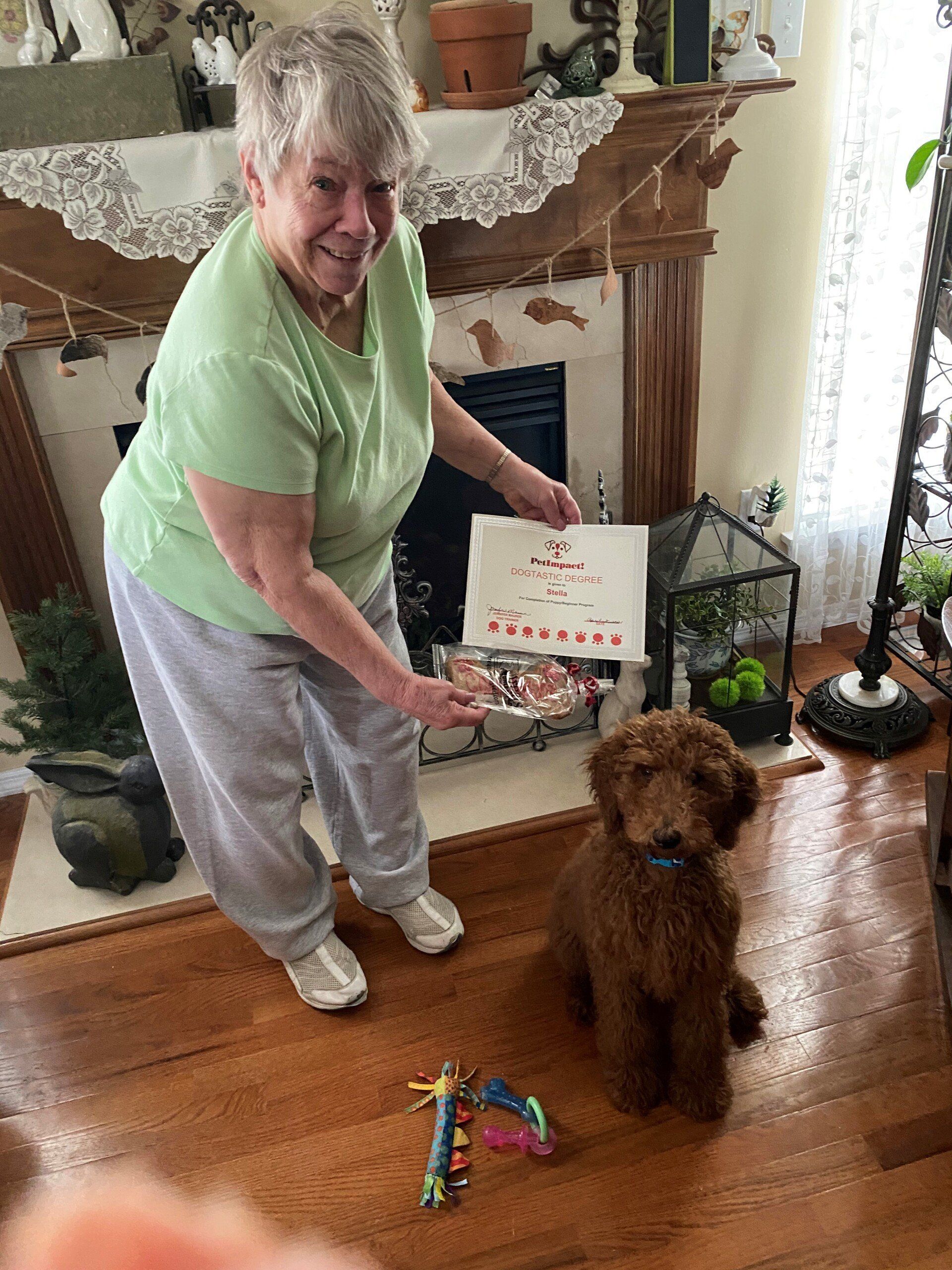 Woman holding treats and a sign, next to a brown dog indoors.