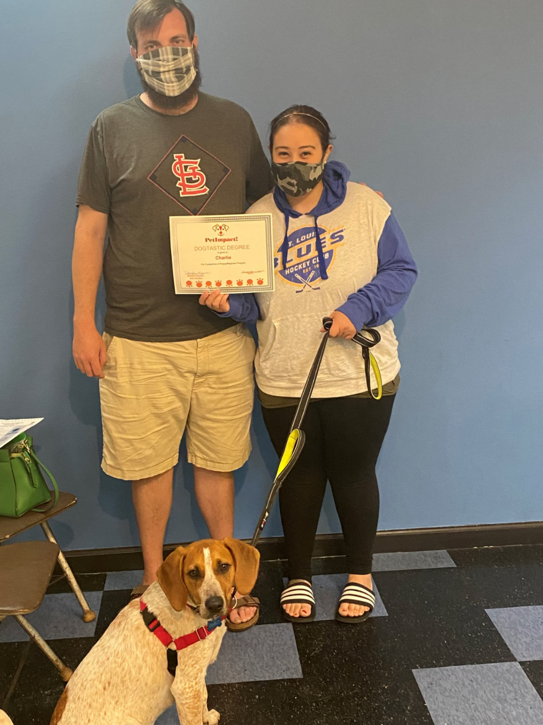 A woman in a hoodie and a man in a t-shirt holding a certificate, with a dog at their feet.