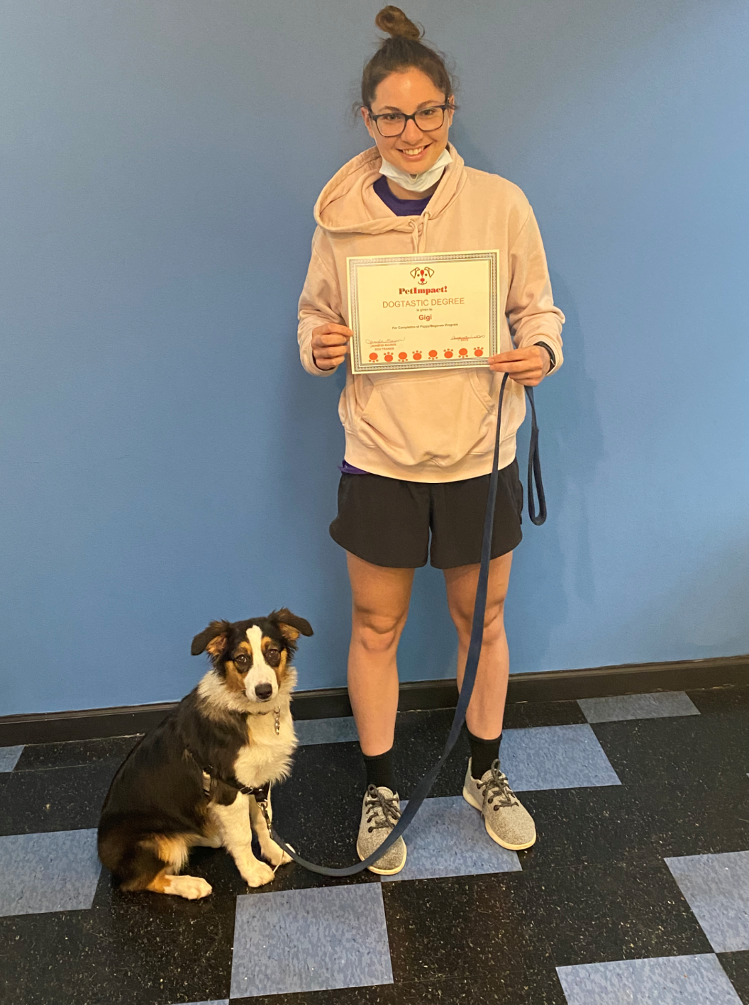 Woman and dog with certificate in front of a blue wall. Woman is smiling, holding the leash and certificate.