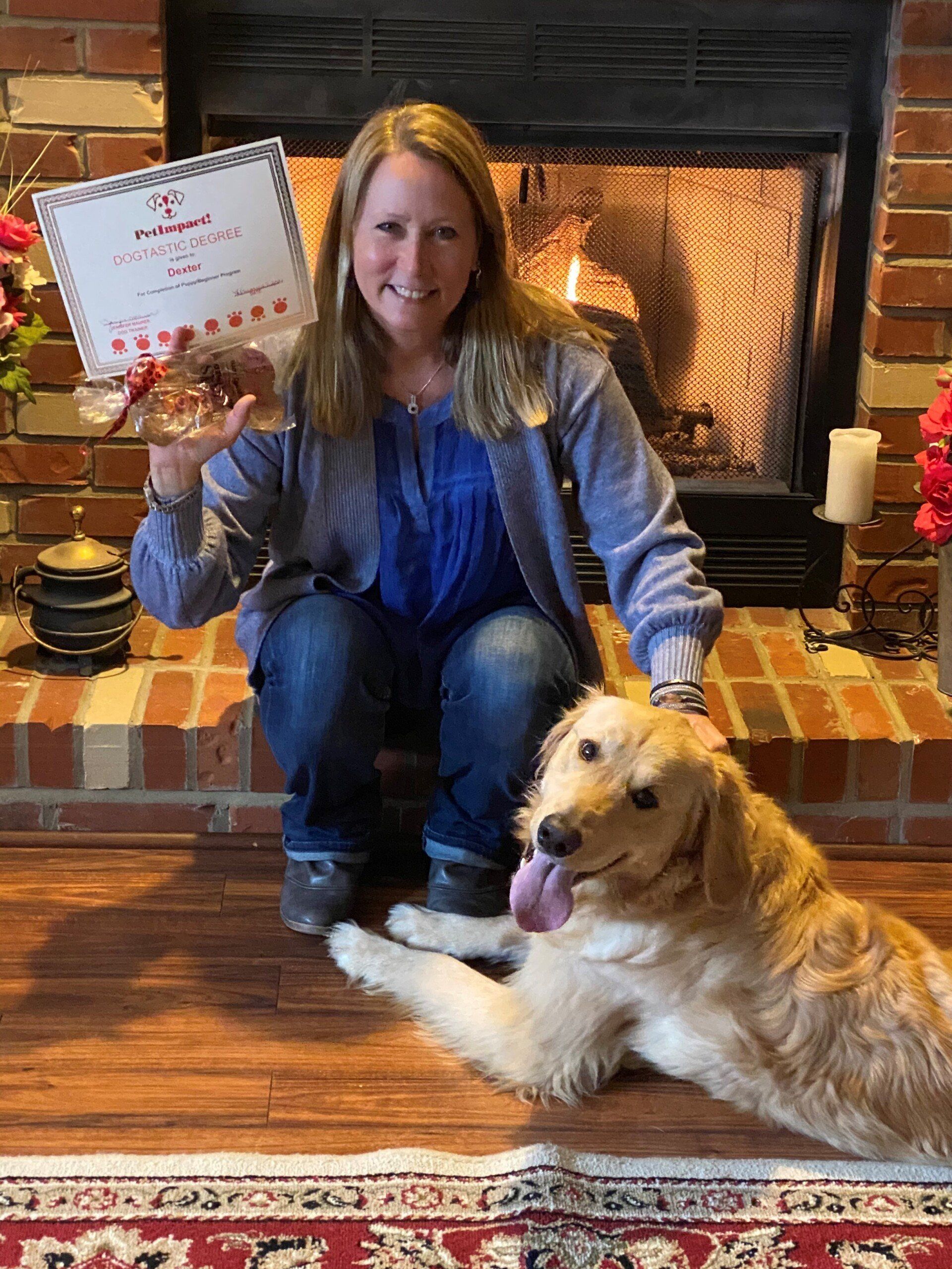 Woman seated with a golden retriever, holding a trophy in front of a fireplace.