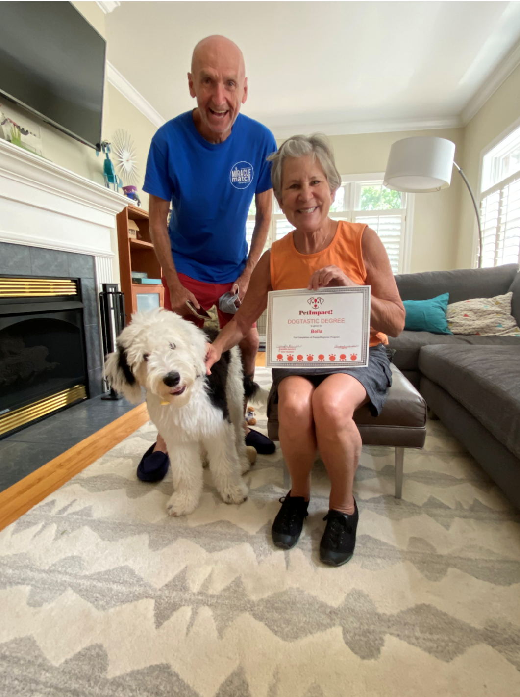 Smiling couple with dog, holding award in a living room.