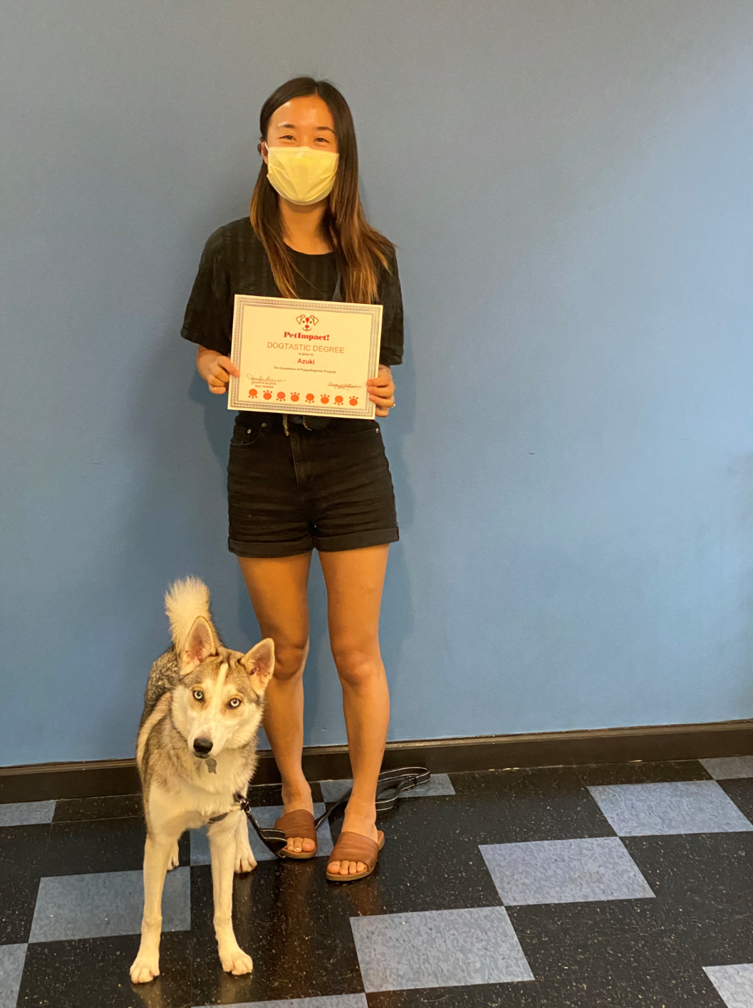 Woman and dog stand in front of a blue wall holding a certificate.