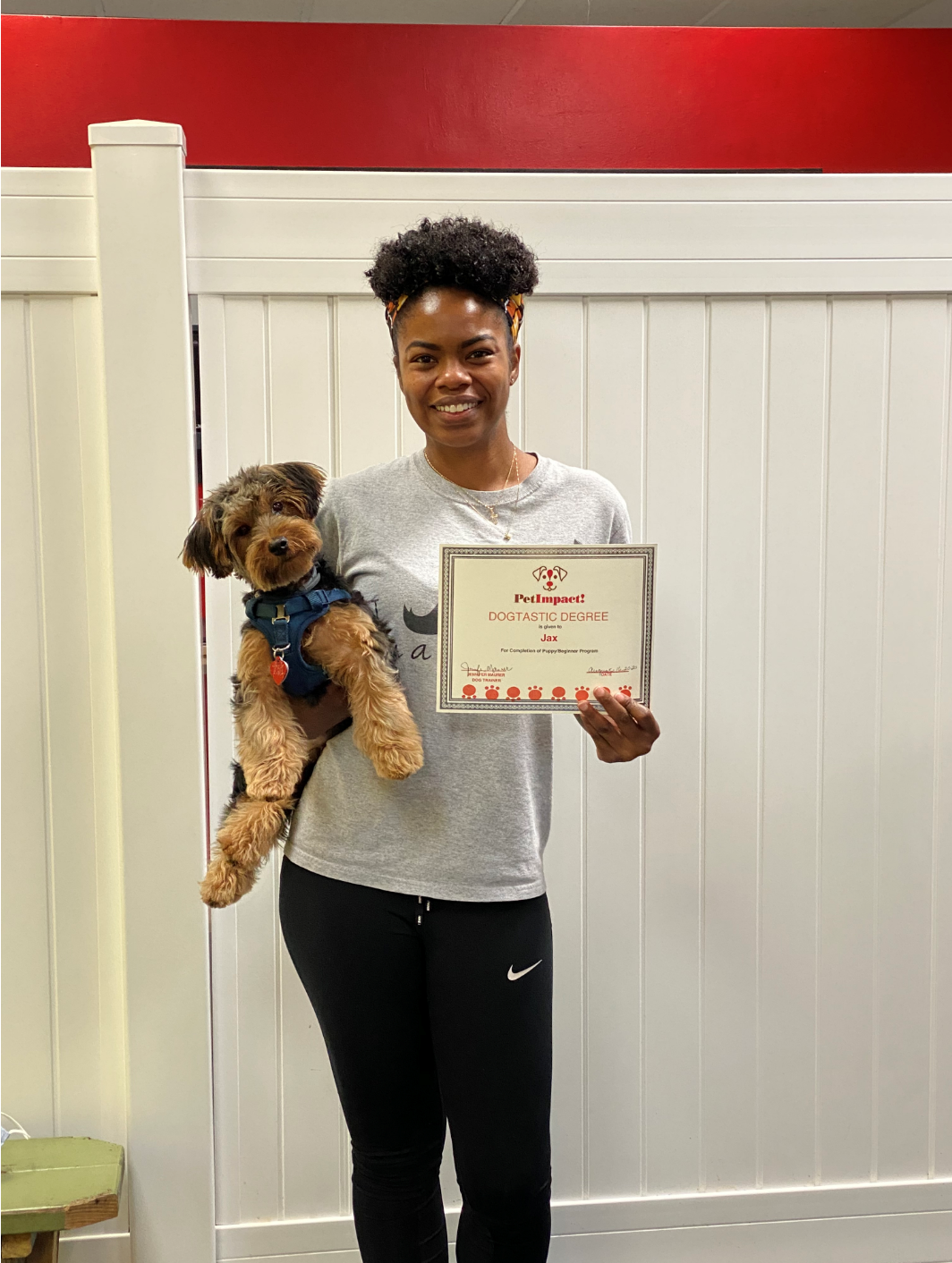 Woman holding a dog and a certificate; standing in front of a white wall with red trim.