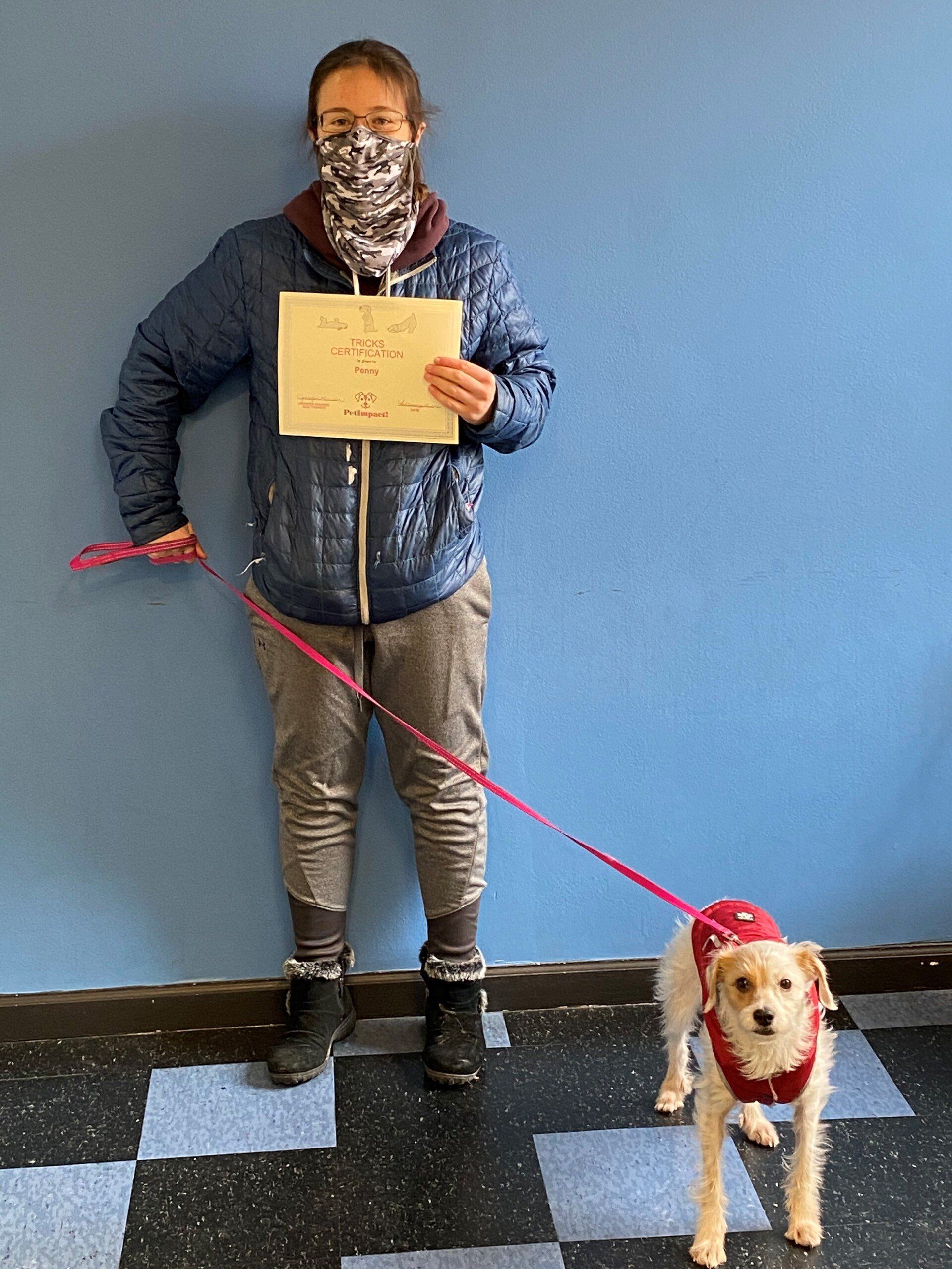 Woman with dog on leash holding paper, standing against blue wall.