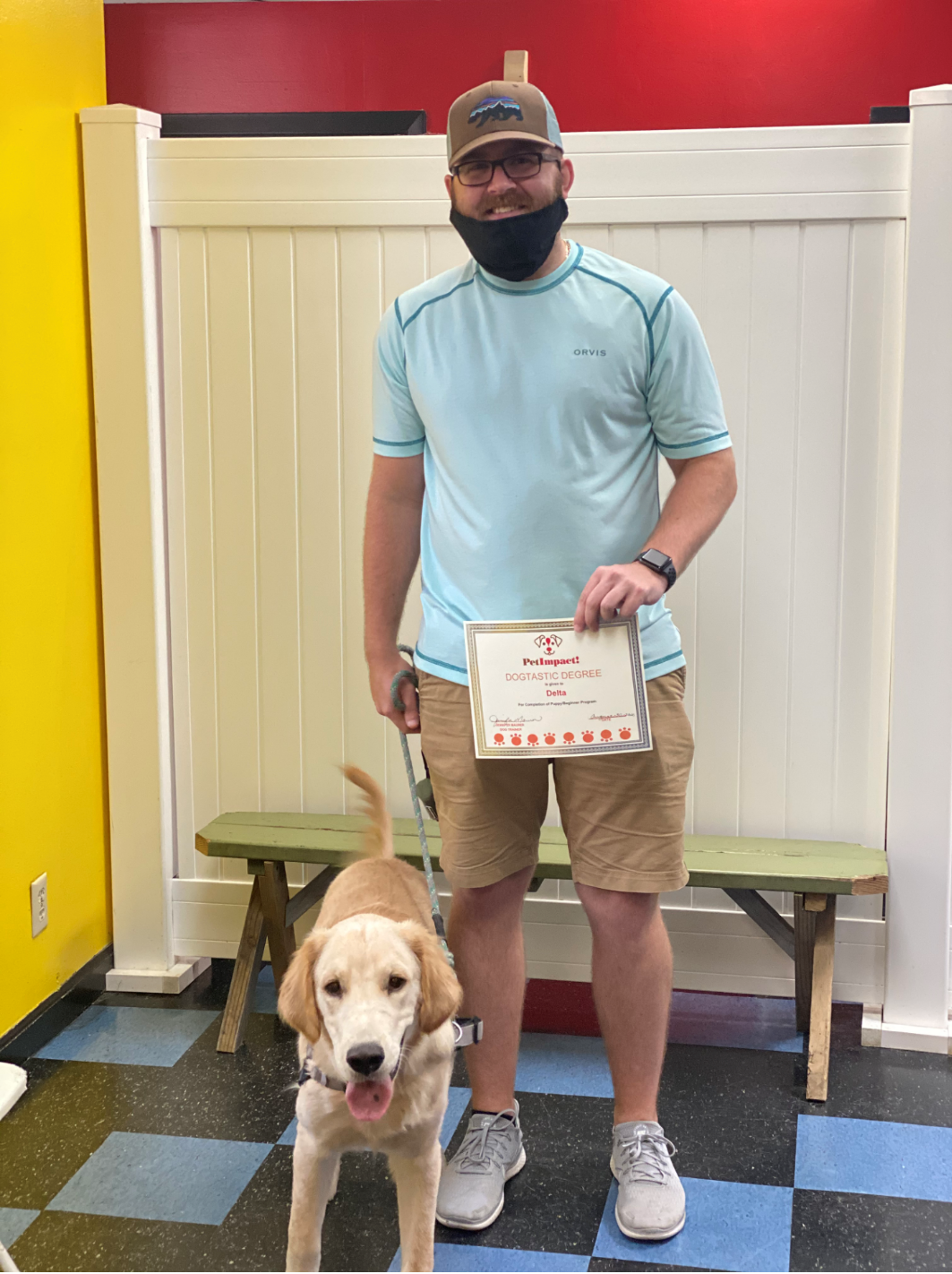 Man holding a certificate stands with a golden doodle dog. Both are in a pet business with a green bench.