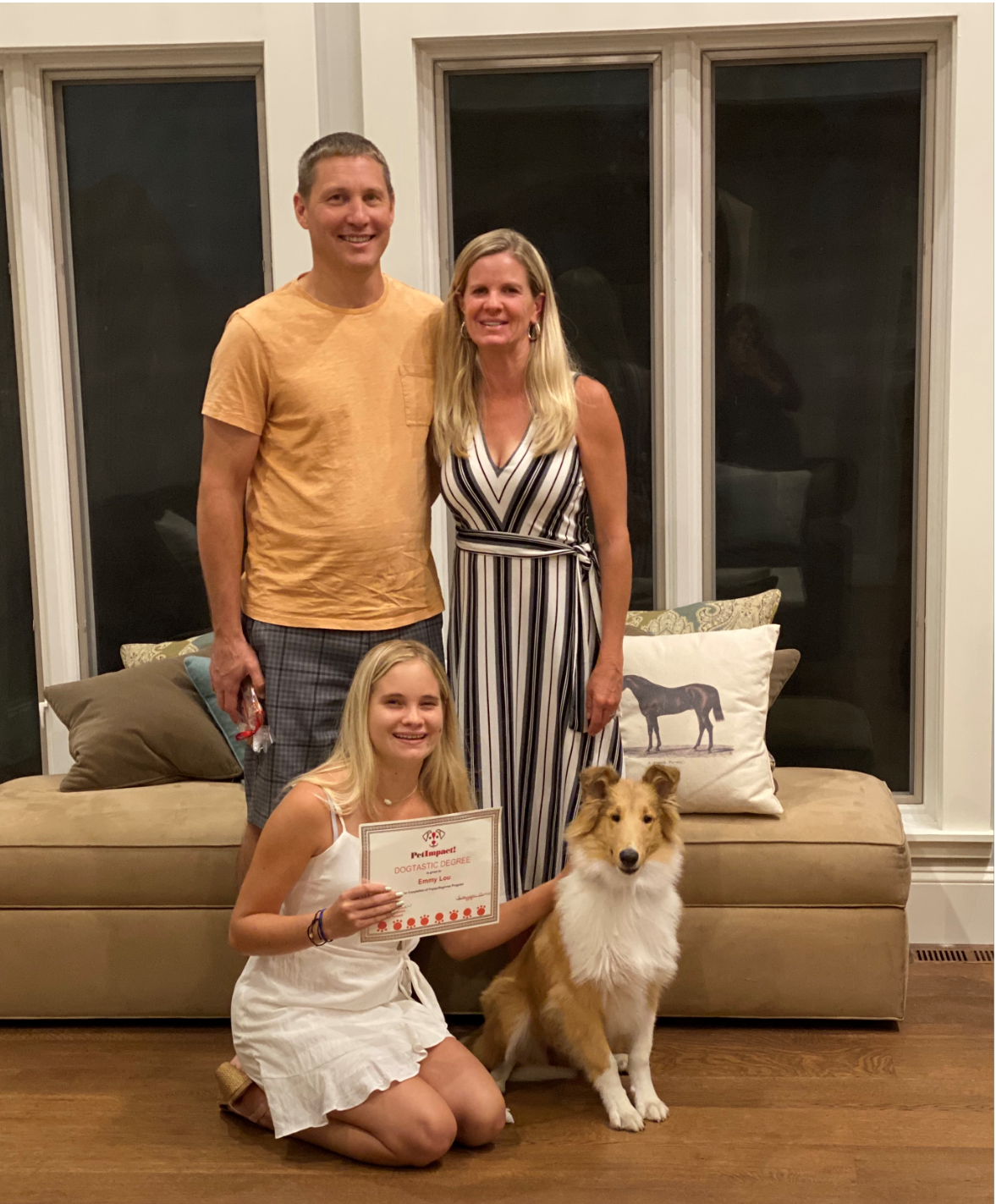 Family with dog poses for photo: woman holding certificate, smiling; two adults behind.