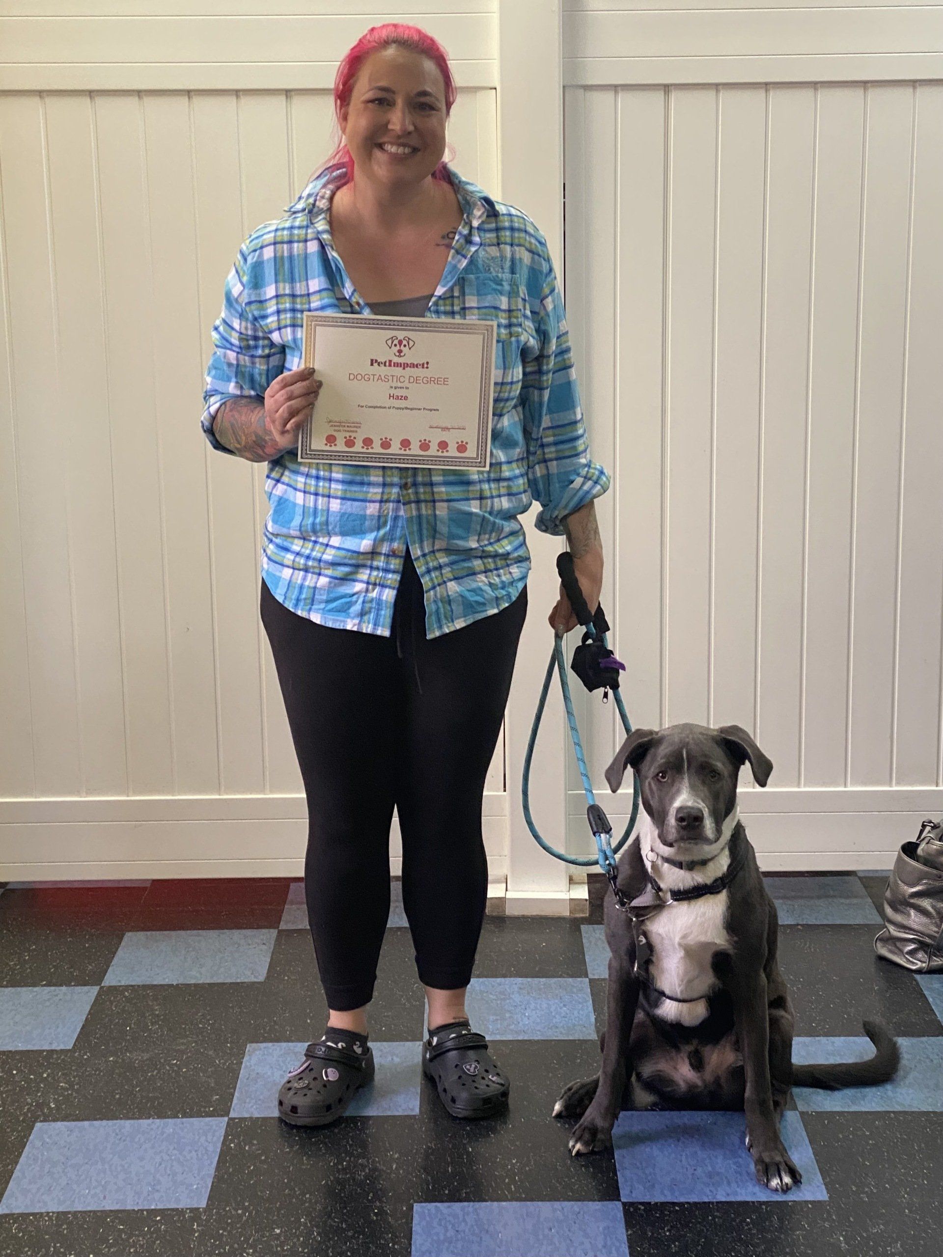 Woman with a dog; the woman holds a certificate. They are in a room with a black and blue tiled floor.