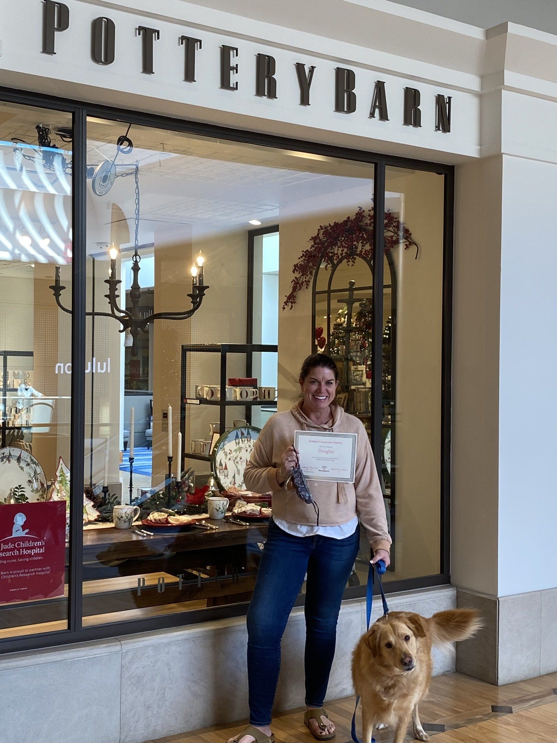 Woman with golden retriever in front of Pottery Barn store, holding paper.