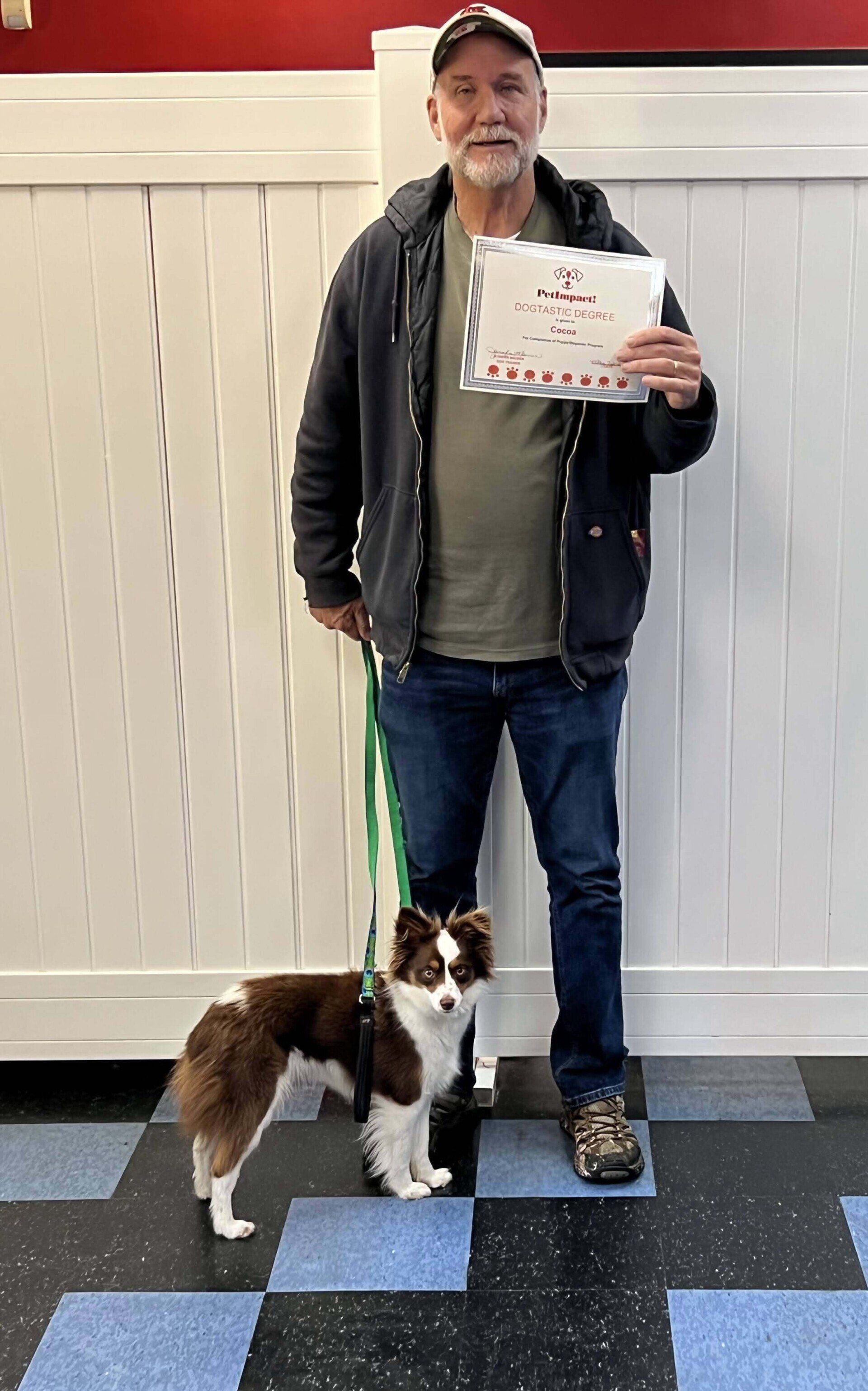 Man and small brown and white dog stand side-by-side, holding a card in front of a white wall.