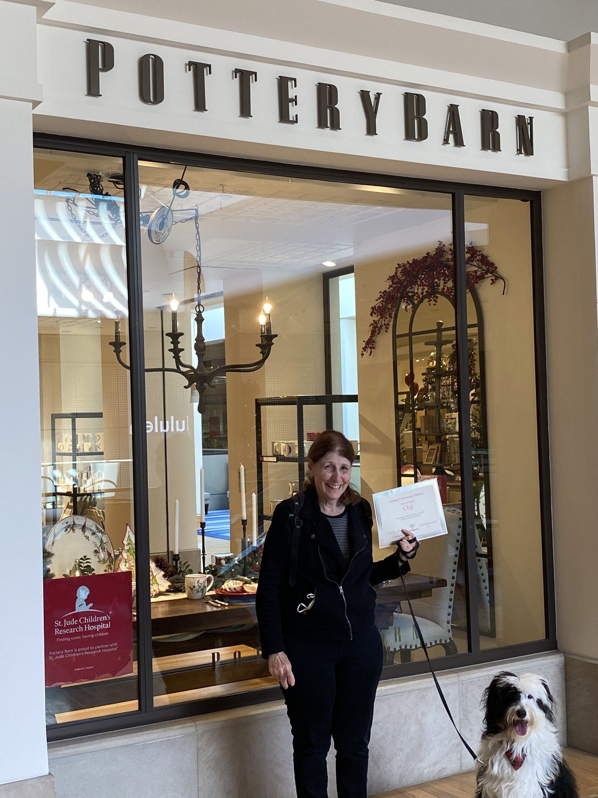 Woman with dog outside Pottery Barn store holding a document.