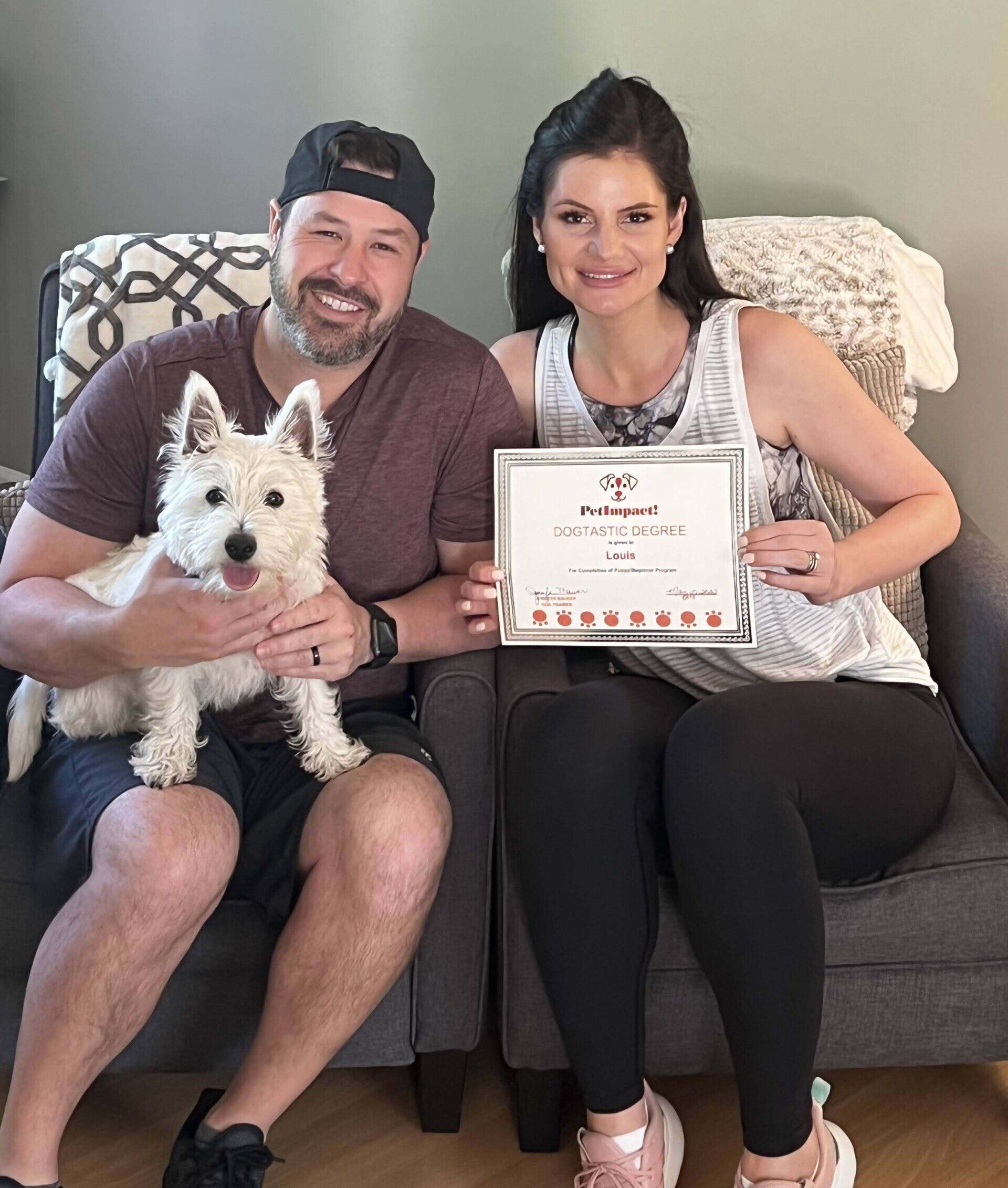 Couple with a white dog sit, holding an award. The woman smiles and the man holds the dog.