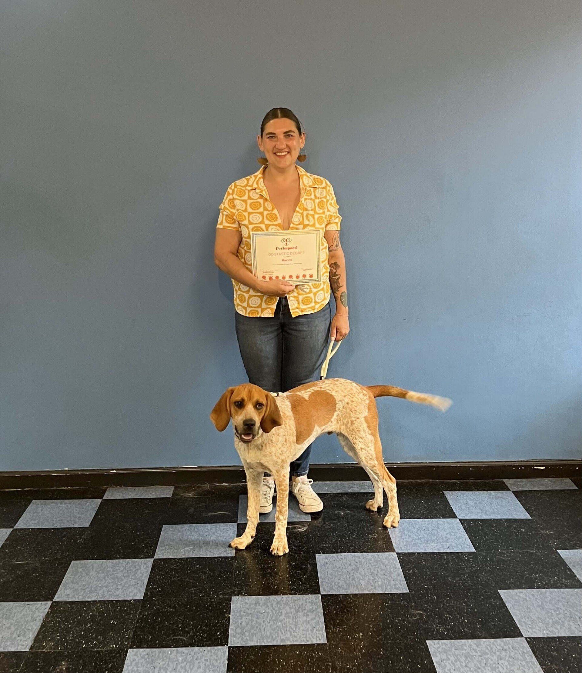 Woman with dog holding a certificate in front of a blue wall and checkered floor.