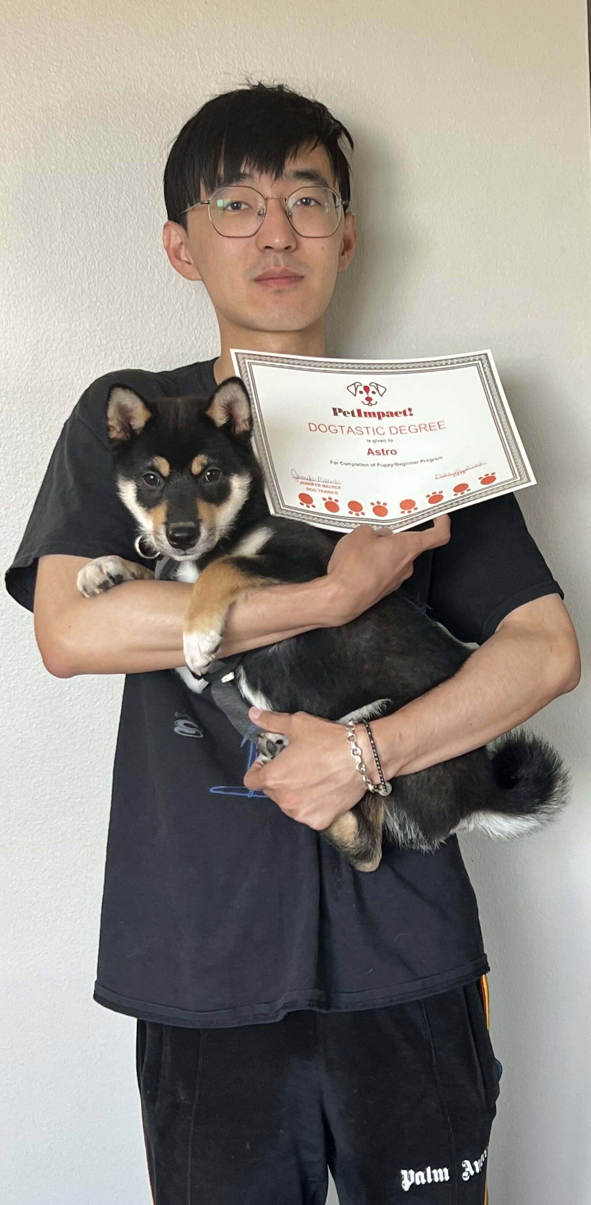 Man holding a black and tan Shiba Inu, holding a certificate.