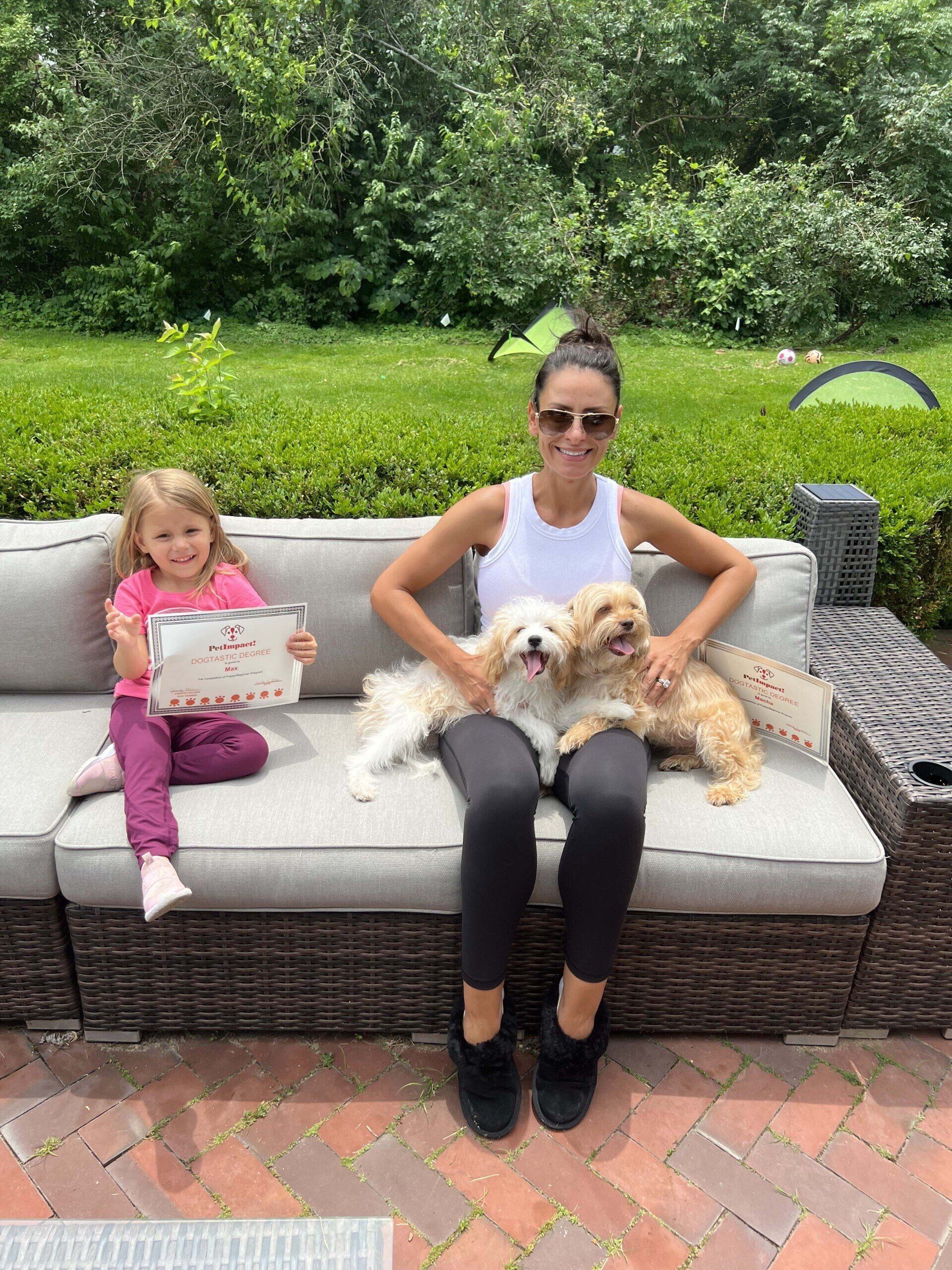 Woman with two dogs and child holding paper on a couch outdoors.