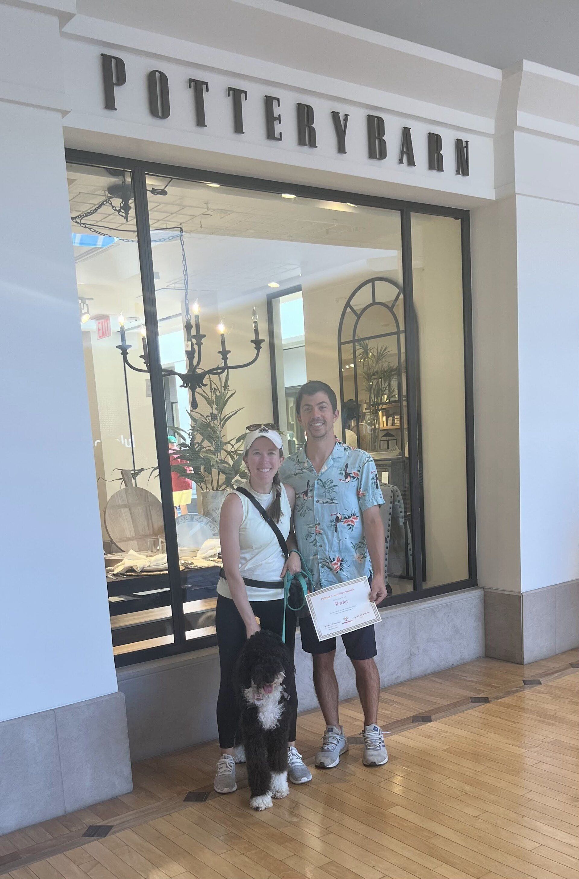Couple with small dog in front of Pottery Barn store. Man holding paper.