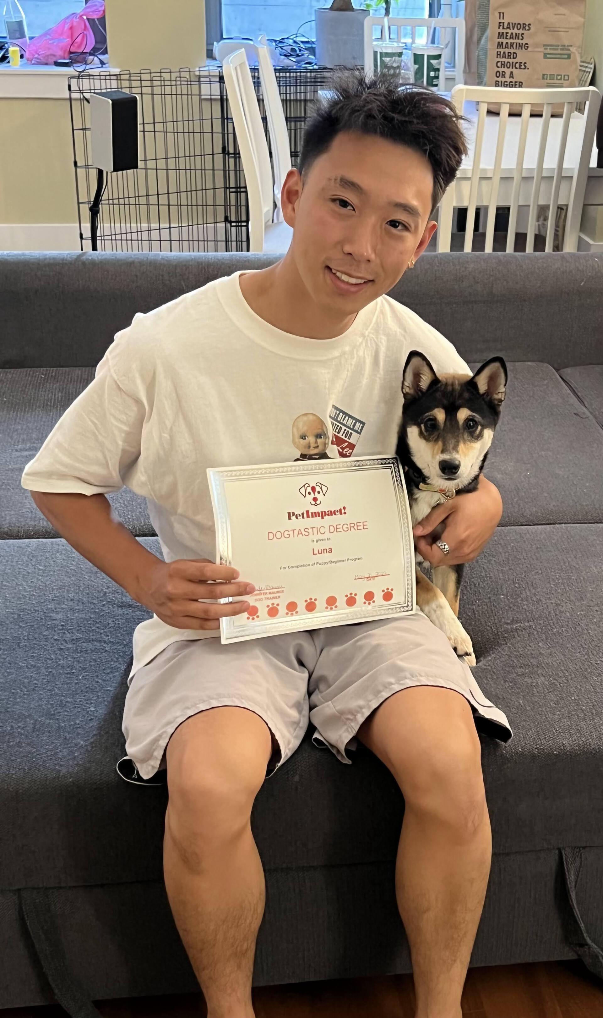 Man and dog seated on a couch, smiling and holding a piece of paper.