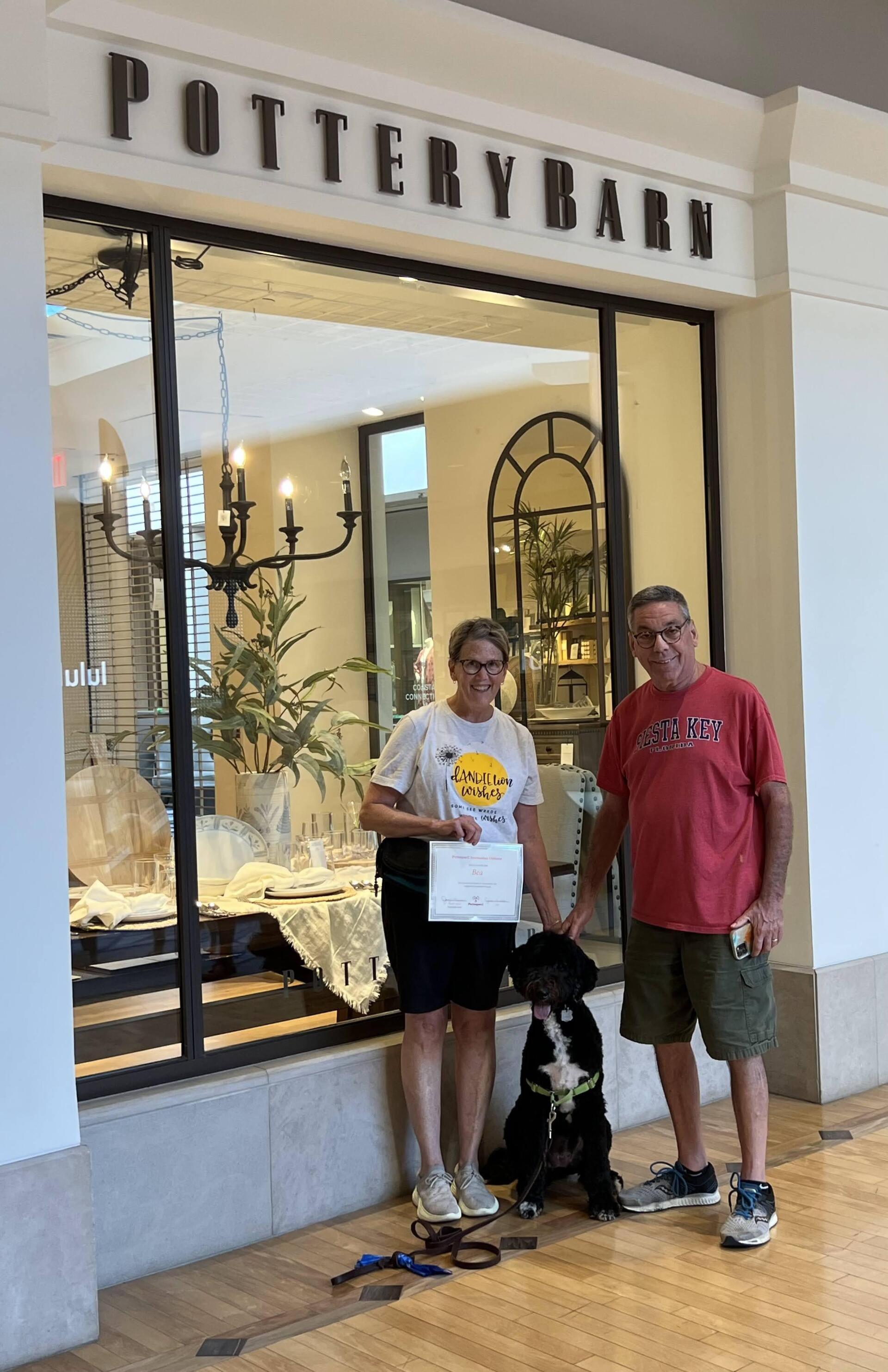 Couple with dog in front of Pottery Barn store. They hold a certificate.