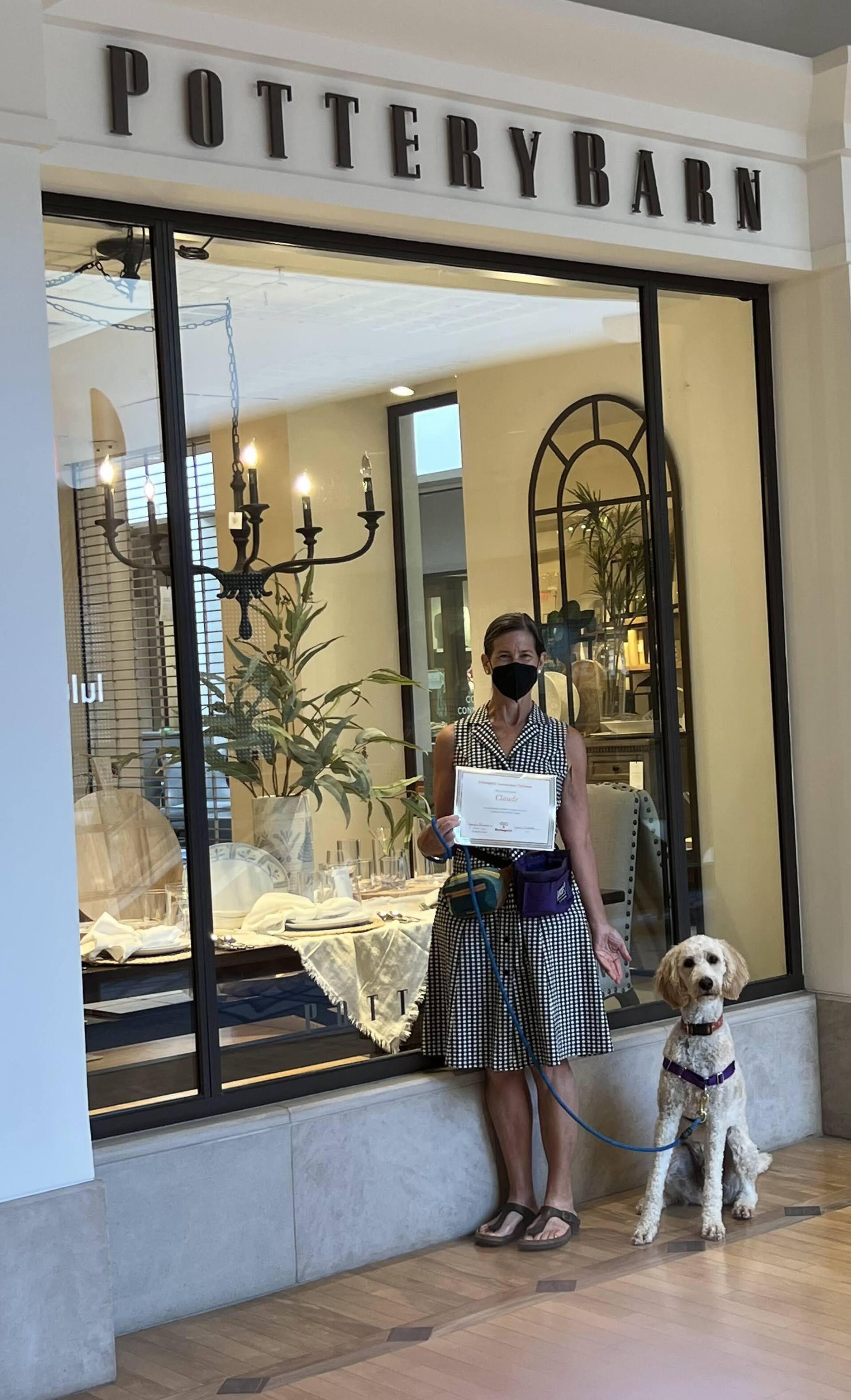 Woman with service dog stands outside Pottery Barn. She holds a paper and smiles.