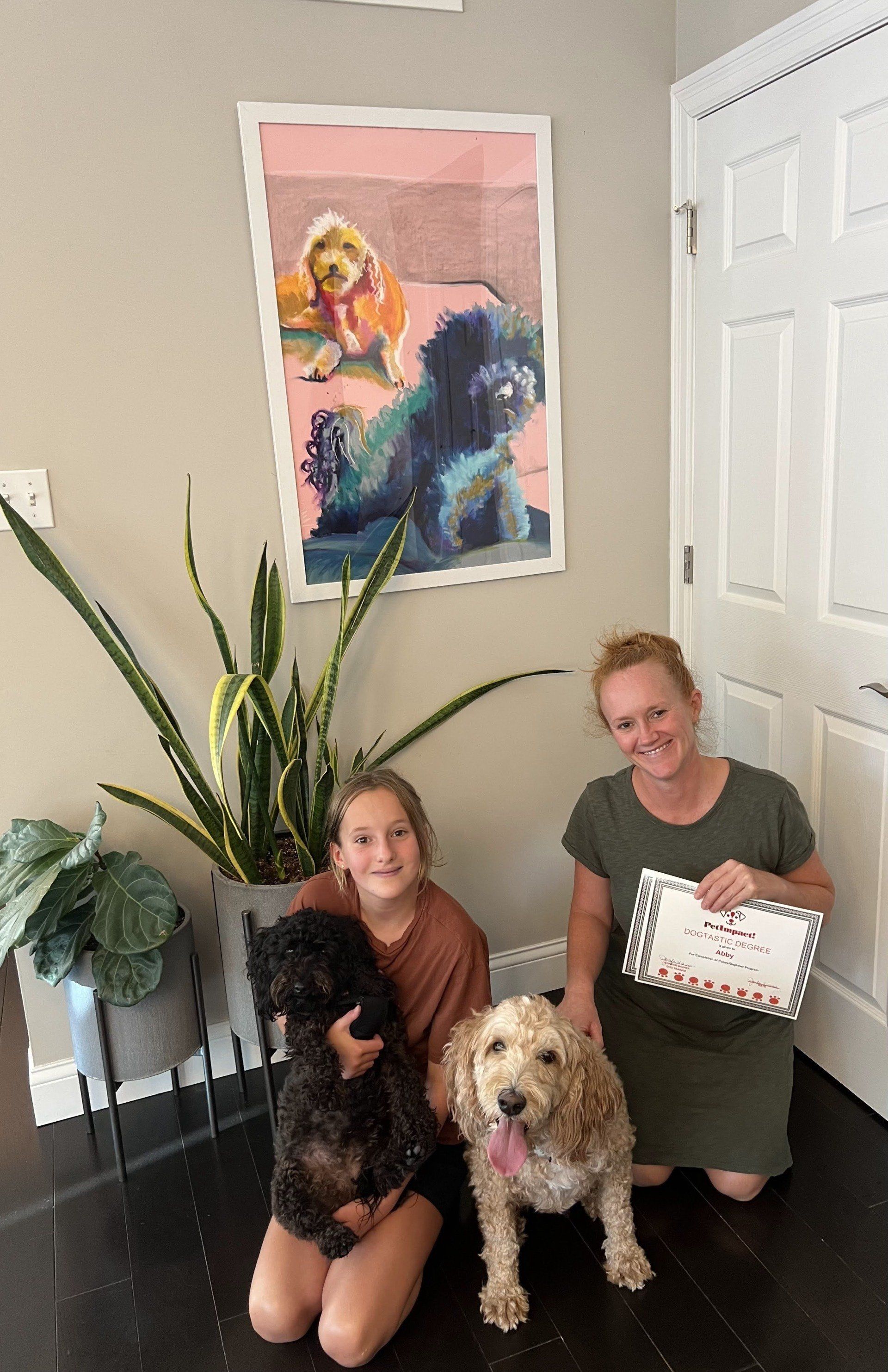 Woman and girl with two dogs pose next to a painting of dogs.