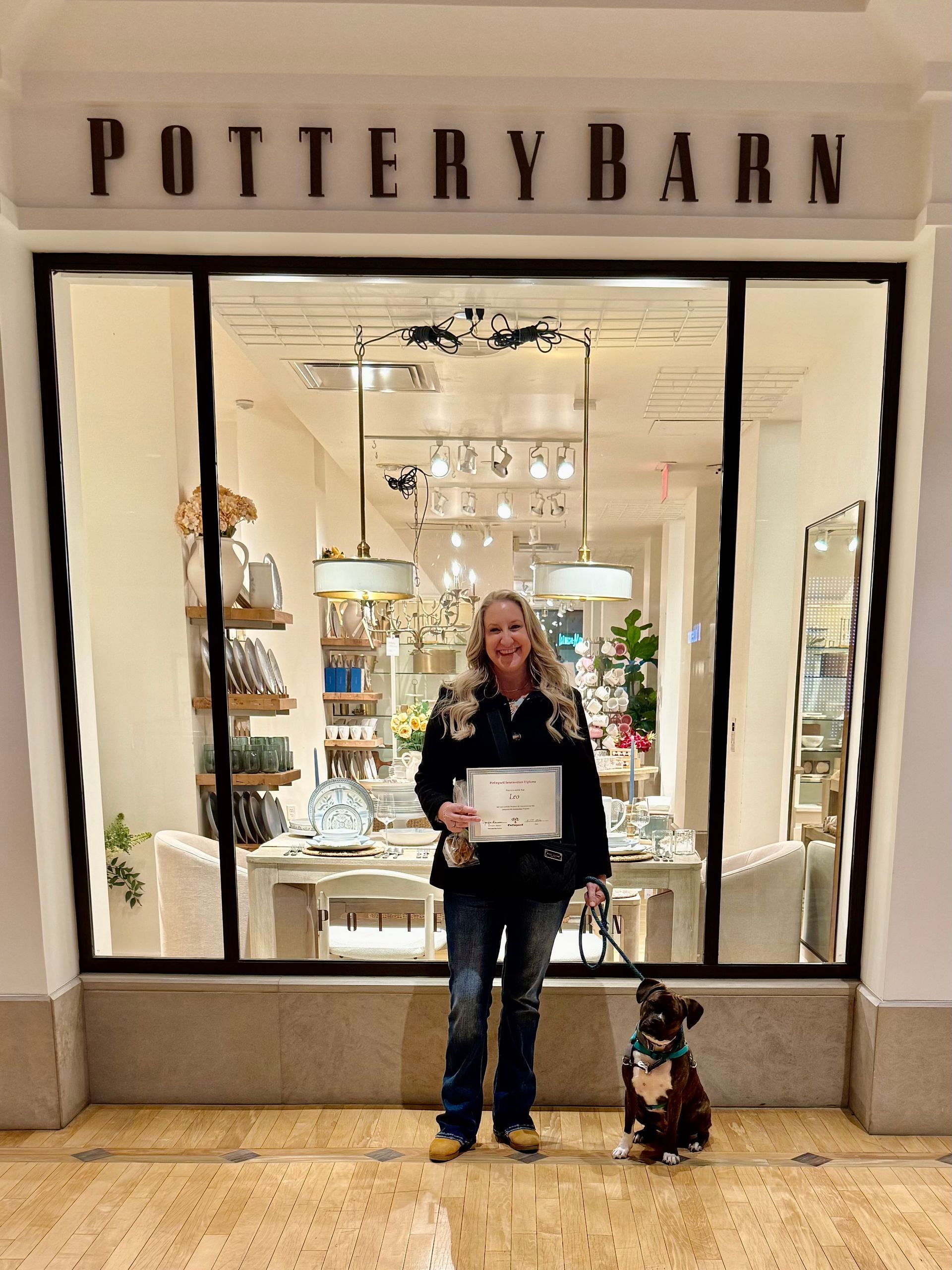 Woman and dog outside Pottery Barn store. Woman holds paper, dog sits. Store has display items.