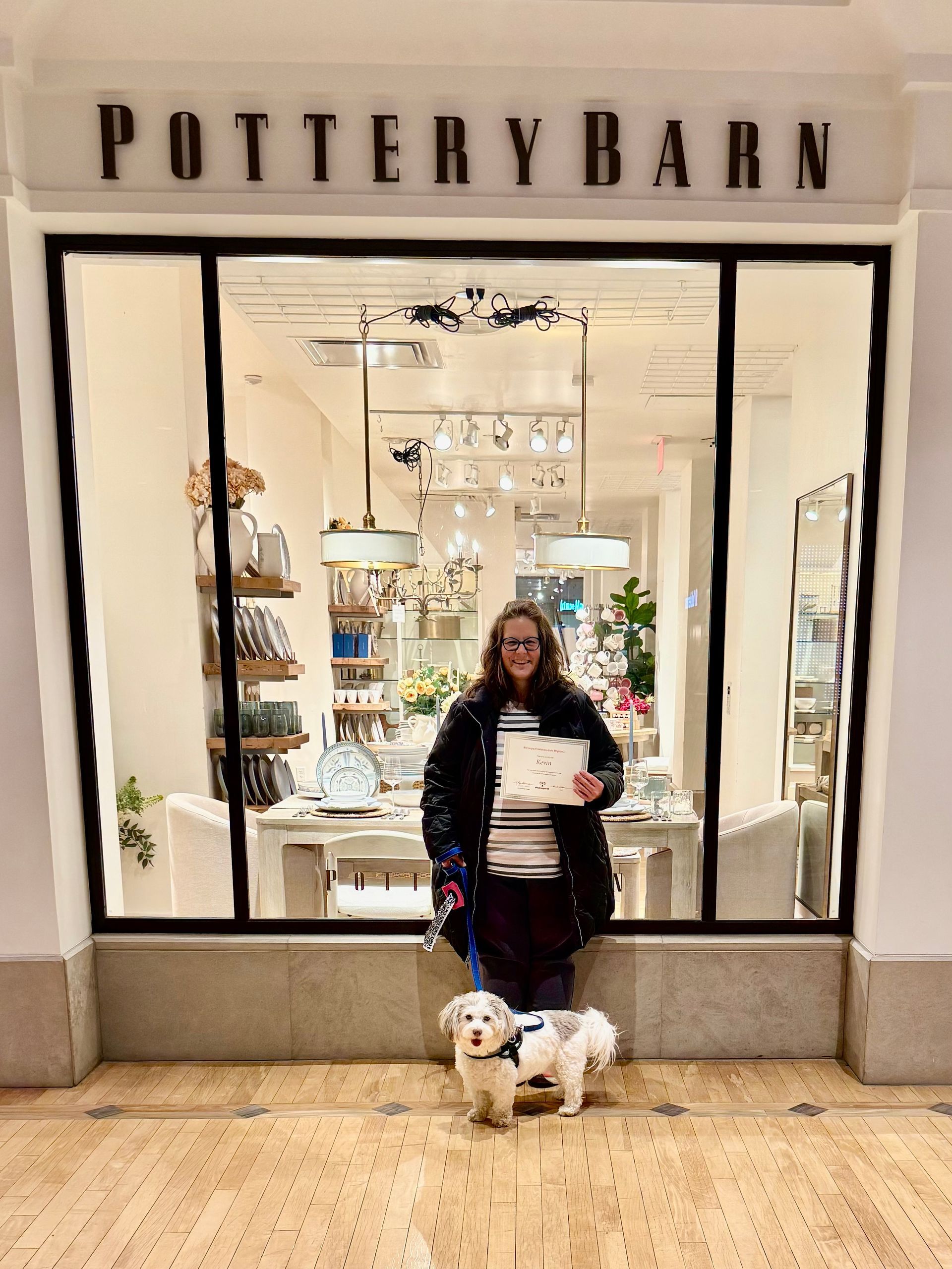 Woman with dog in front of Pottery Barn storefront, holding paper. Storefront has display of items inside.