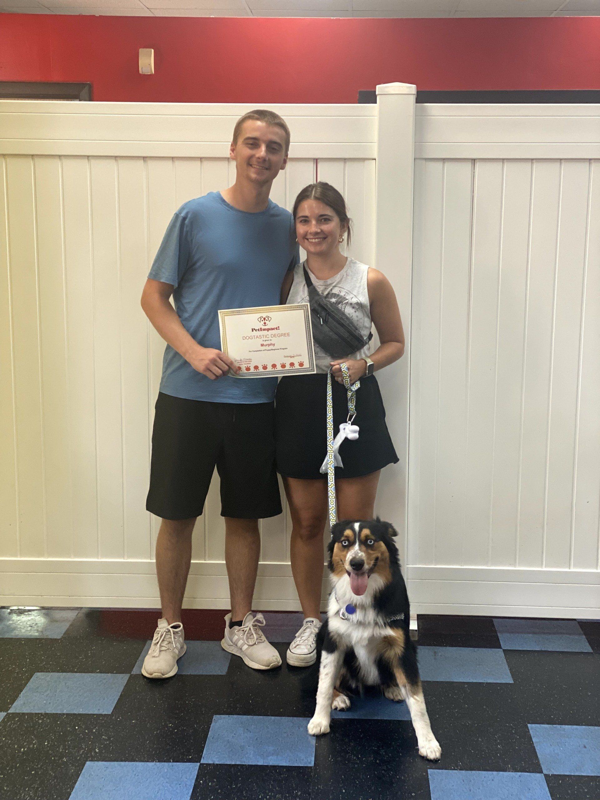 People holding certificate with a dog; the couple poses with the dog.