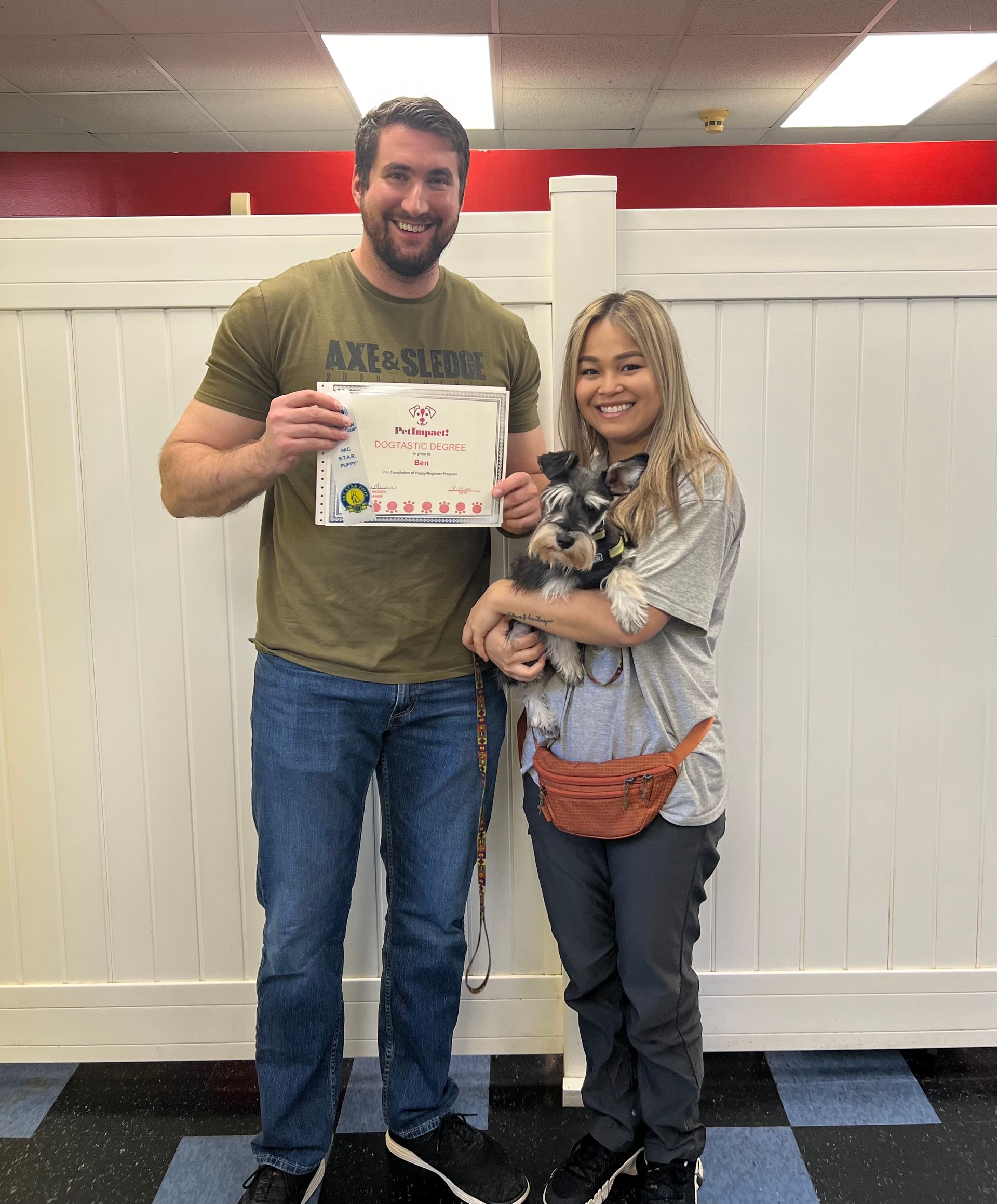 A man and a woman are standing next to each other holding a dog and a certificate.