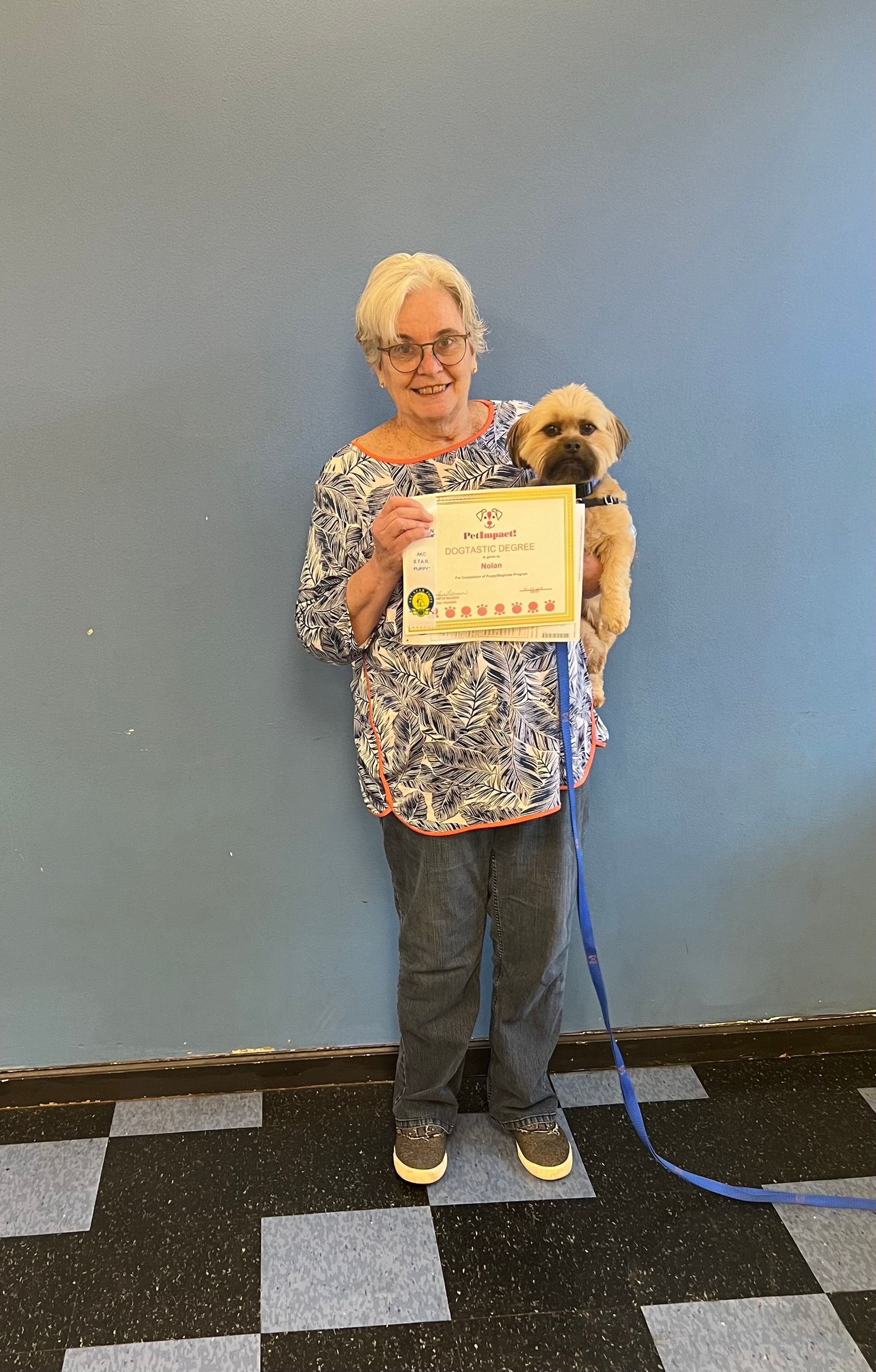 A woman is holding a small dog and holding a certificate.