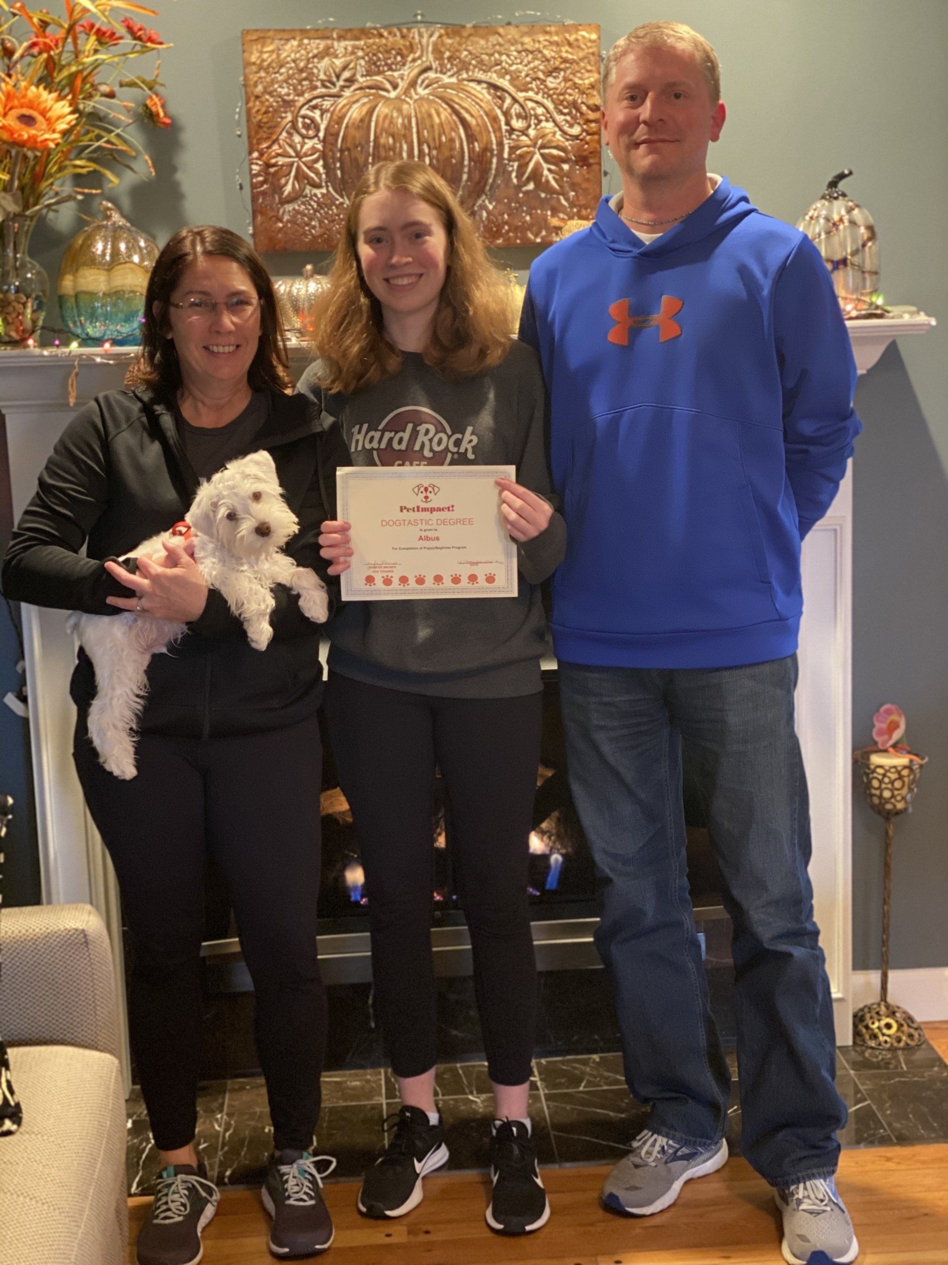 Family of three with a small white dog; a woman holds the dog, a teen holds a certificate.