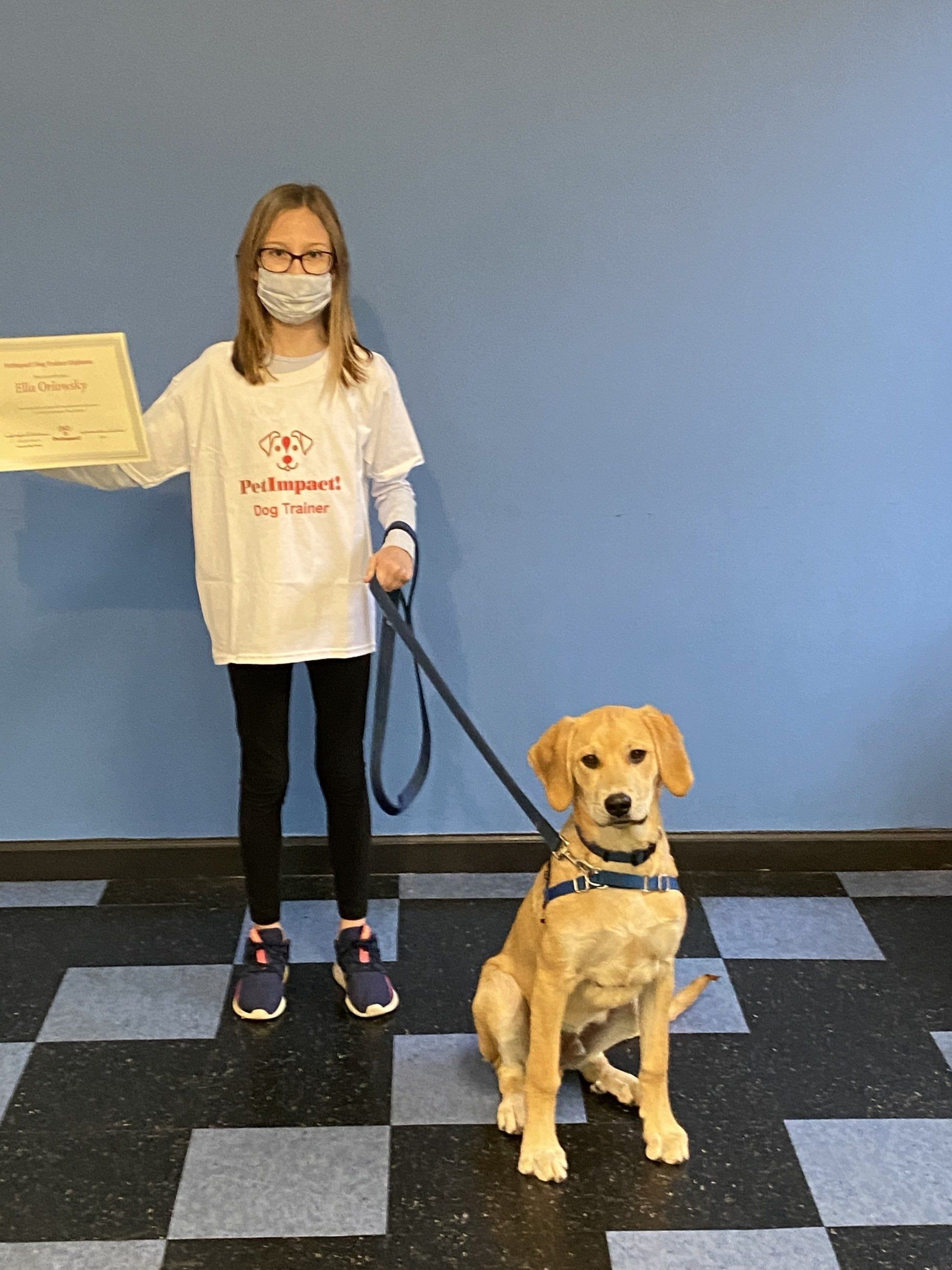 Girl in a t-shirt and mask with a golden retriever puppy, holding a certificate.