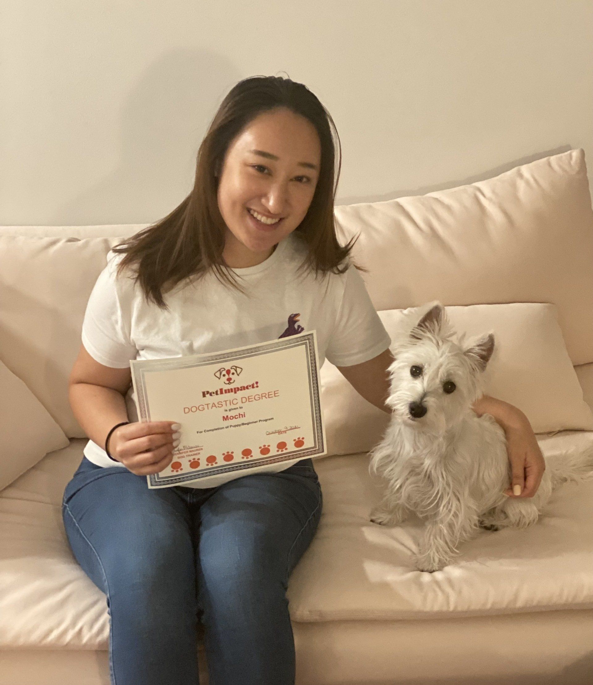 Woman and small white dog on a couch, holding a certificate. Both are smiling.