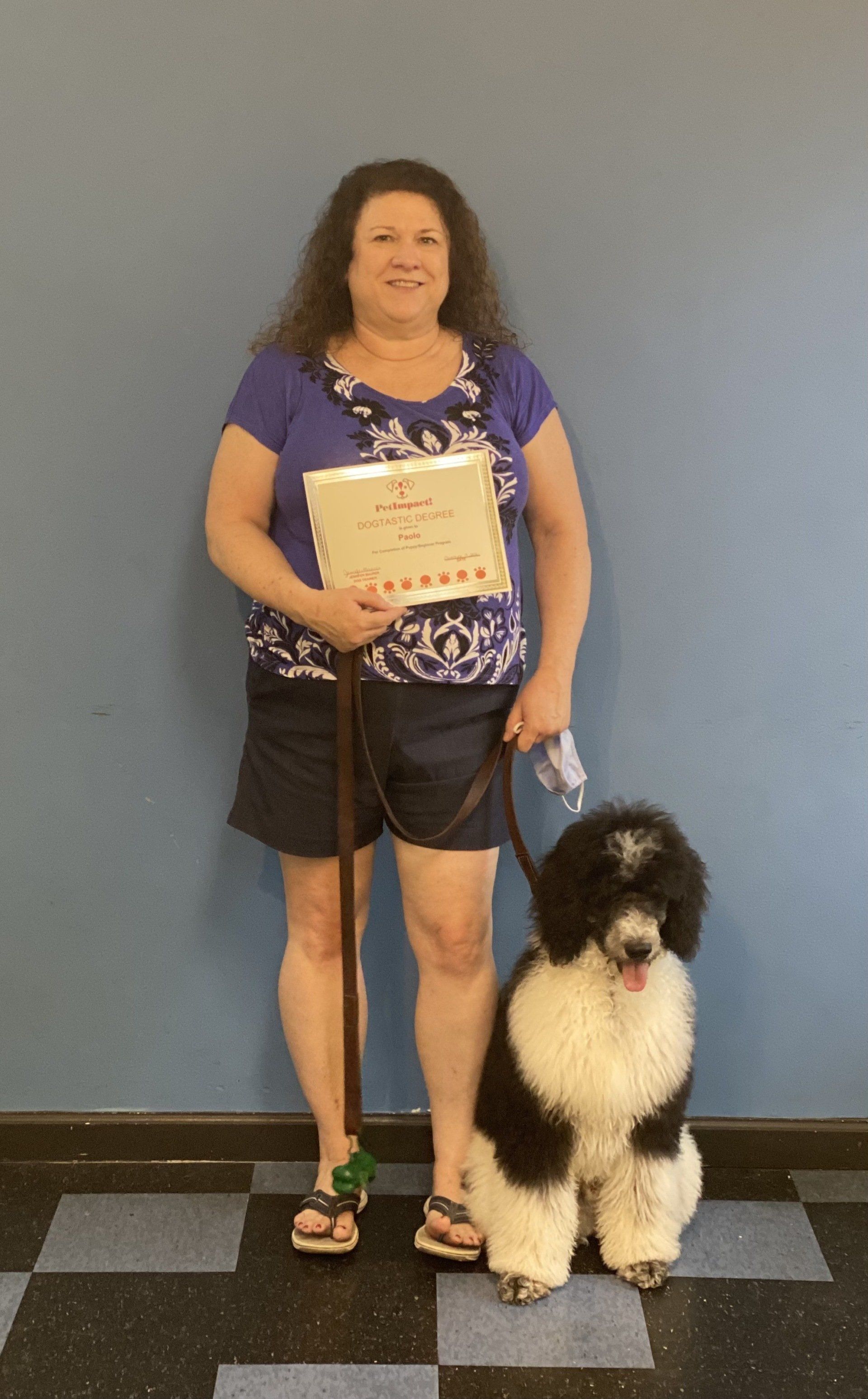 Woman holding award, posing with a black and white poodle. Blue wall, checkered floor.