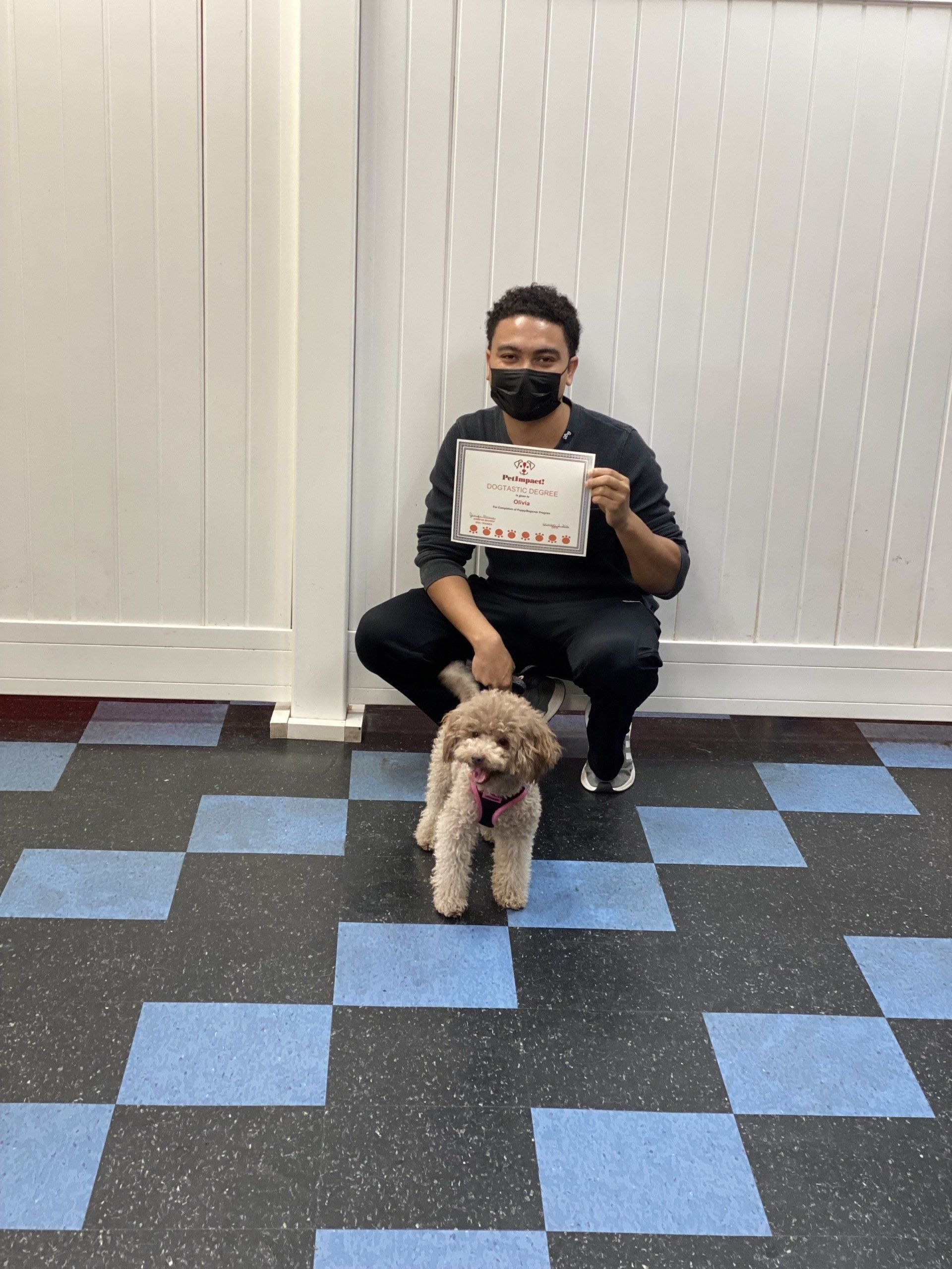 Man kneeling with a dog, holding sign. Blue and black checkered floor, white wall.